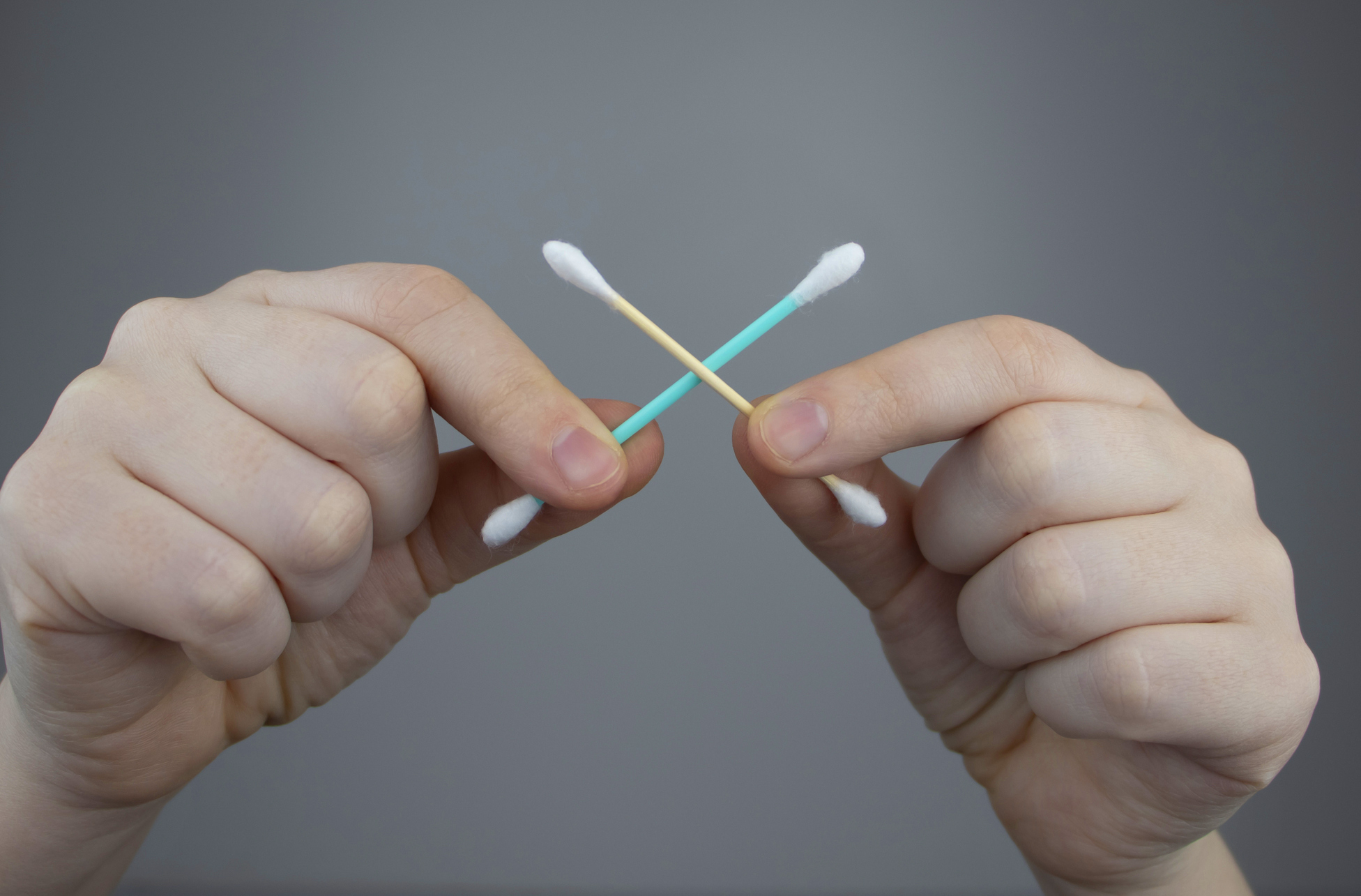 Two hands holding a cotton swab in an X formation.