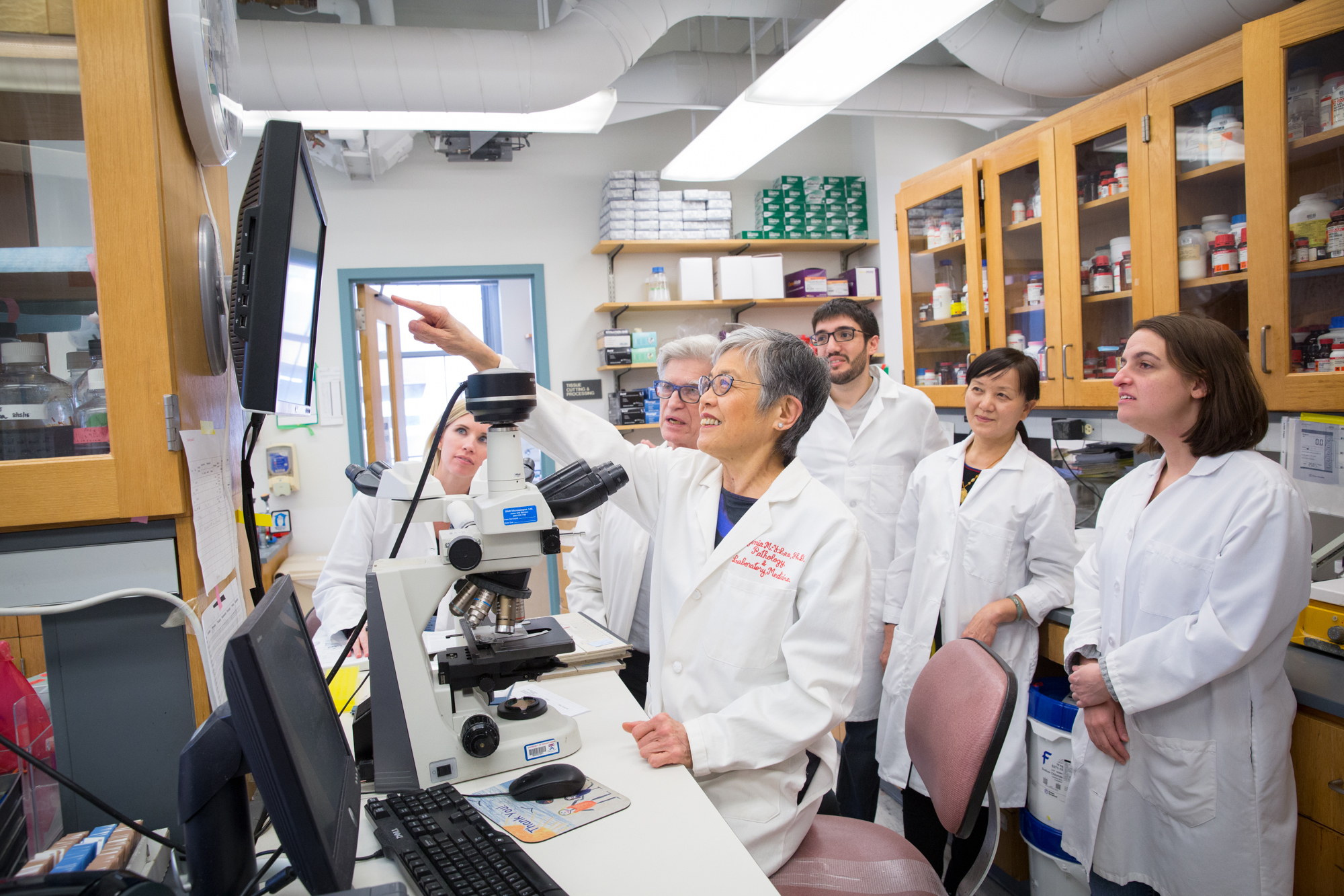 Virginia Lee in her lab points at a computer screen with a team of lab members around her.