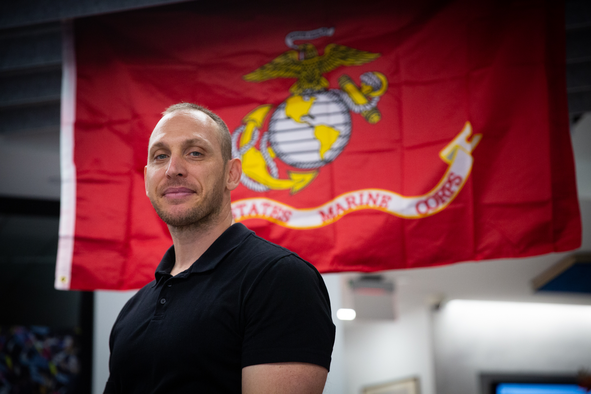 Aaron Autler stands in front of a flag reading "United States Marine Corps"