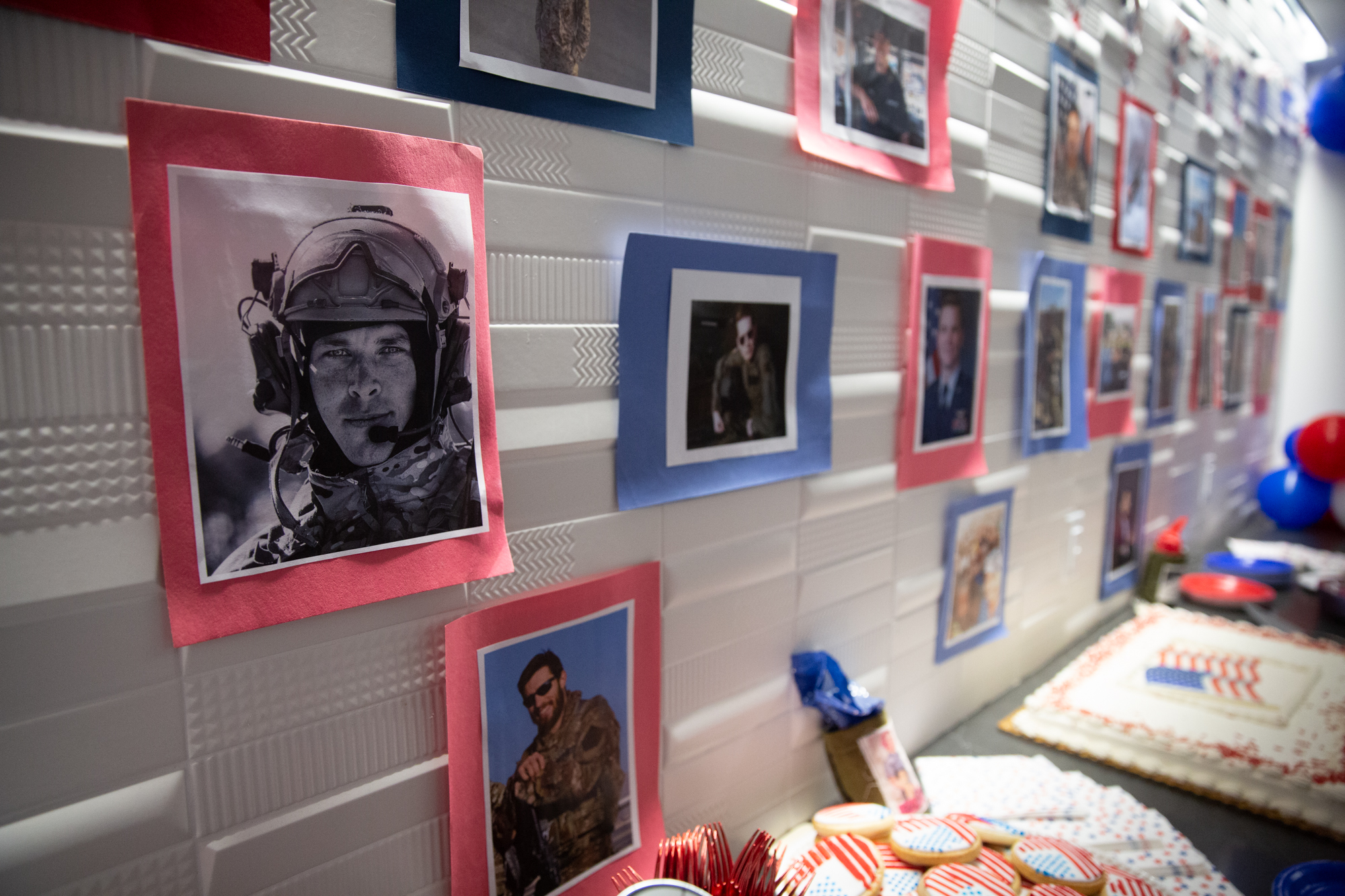 A wall of photographs show student veterans in uniform. American flag themed cookies and cakes are below
