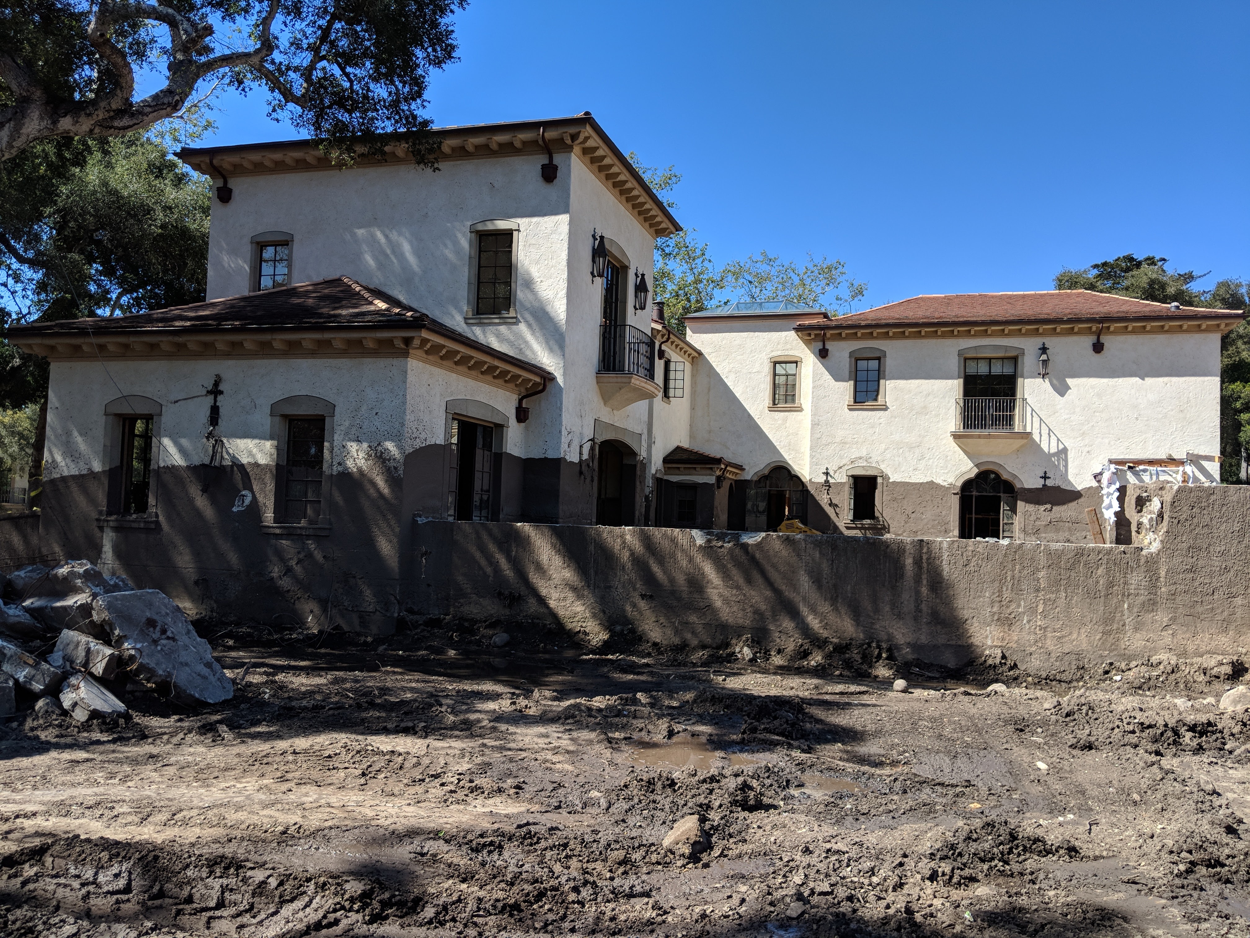 A large white Spanish-style home with a stain of mud coming halfway up the first story