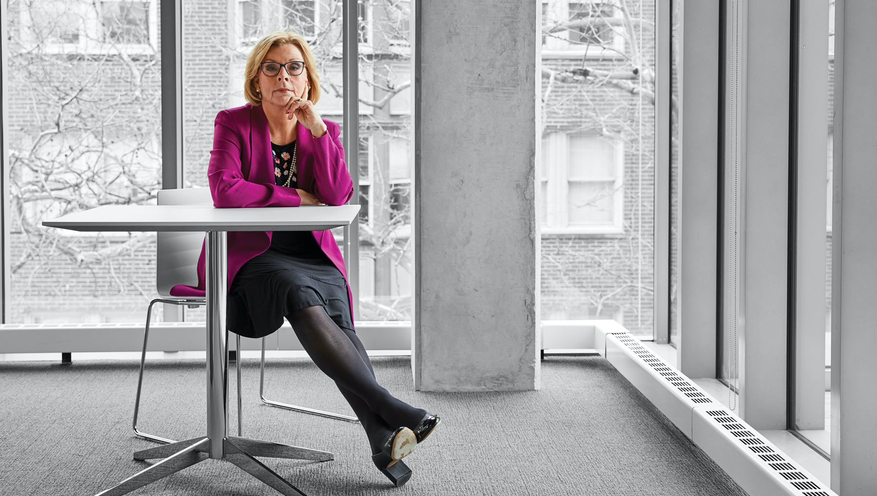 Marci Hamilton sits at a table beside large windows overlooking campus.