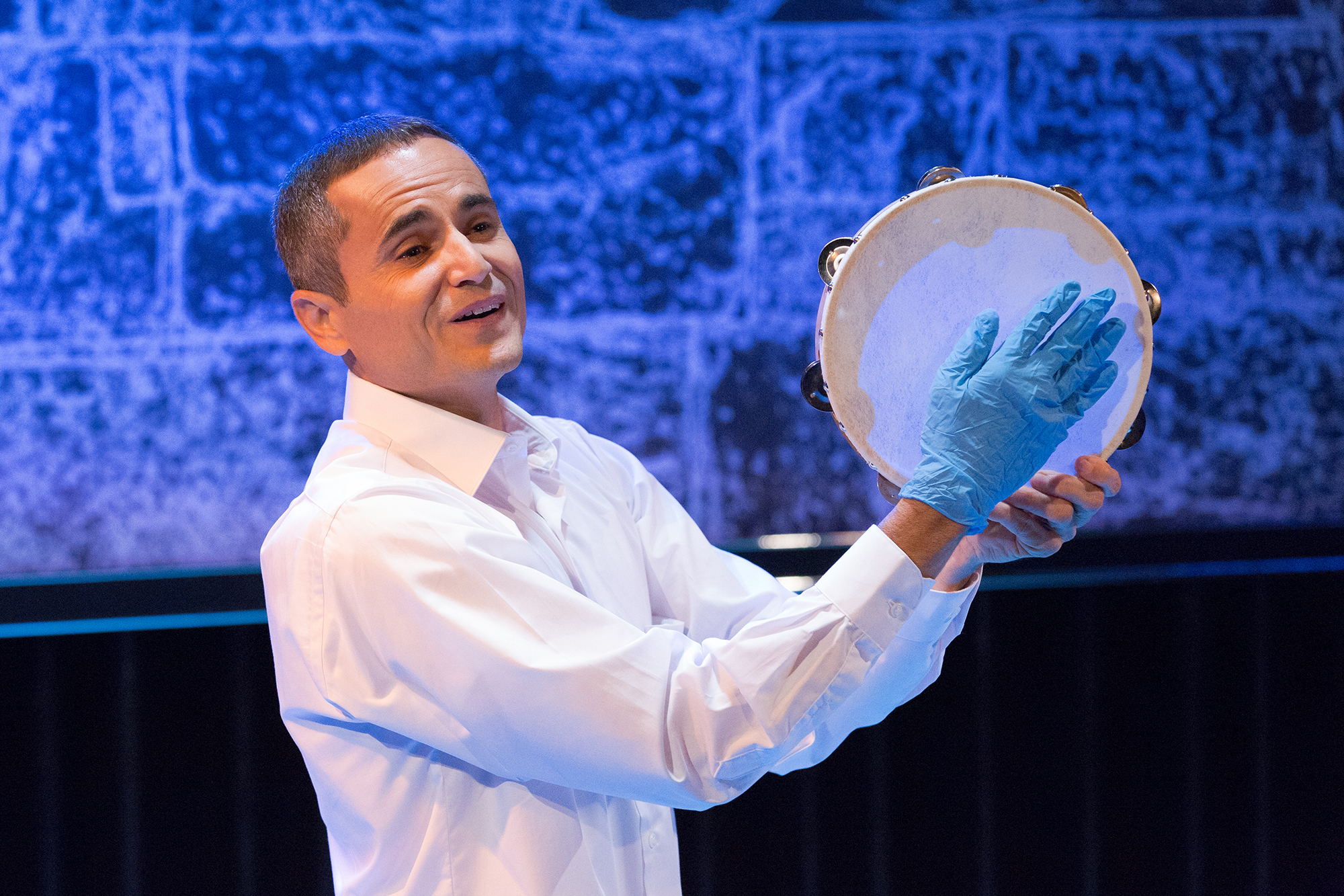 Ibrahim Miari performing on stage wearing a latex glove and holding a drum.