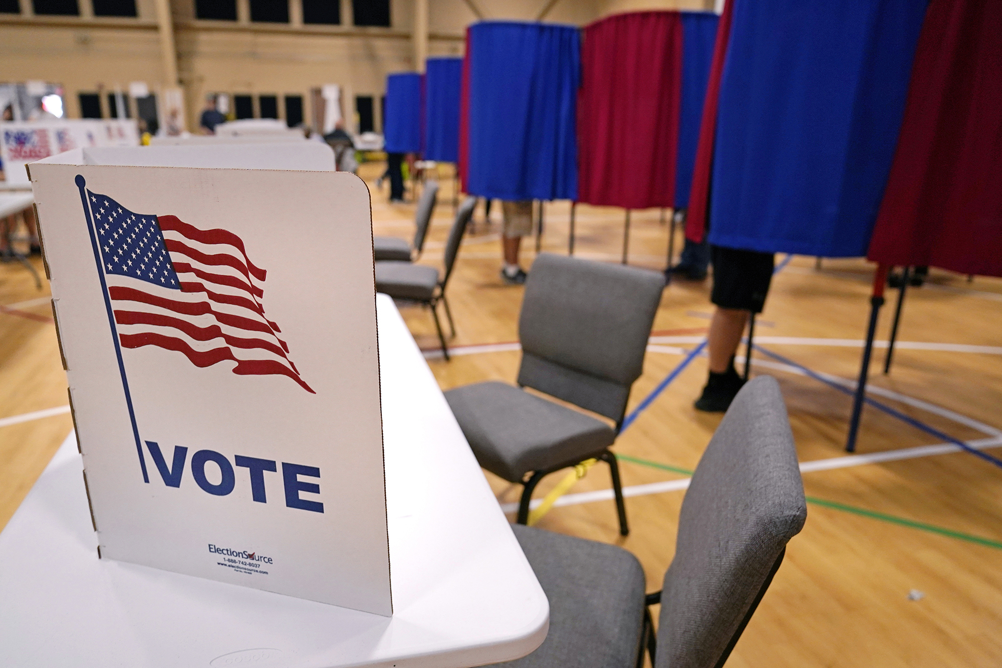 Voting booth with a picture of an American flag on it, with other curtained booths behind it in alternating red and blue