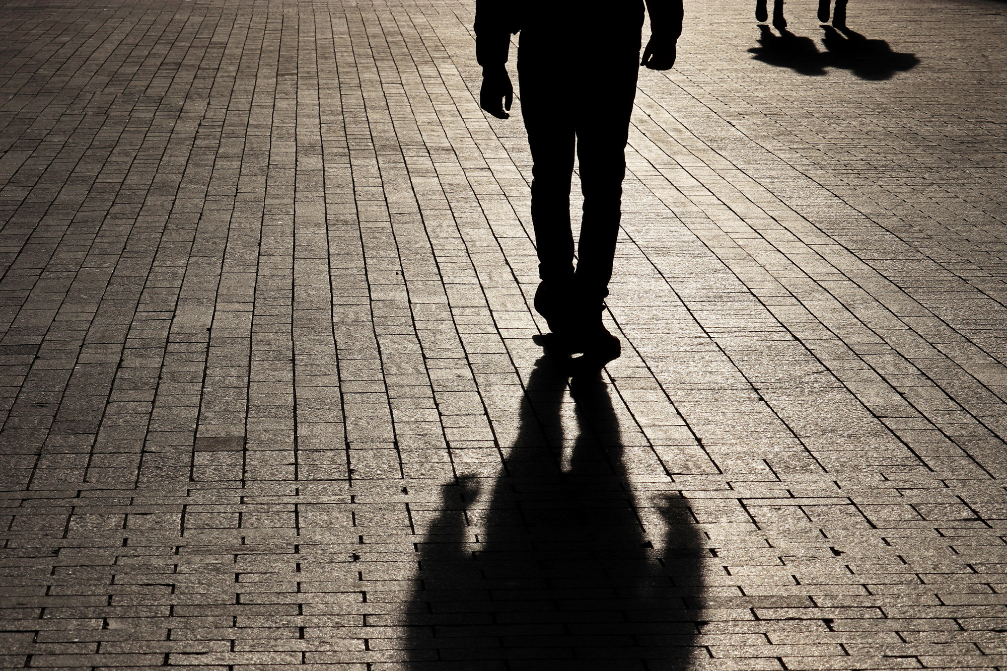A shadowy figure walking away on a brick street. 
