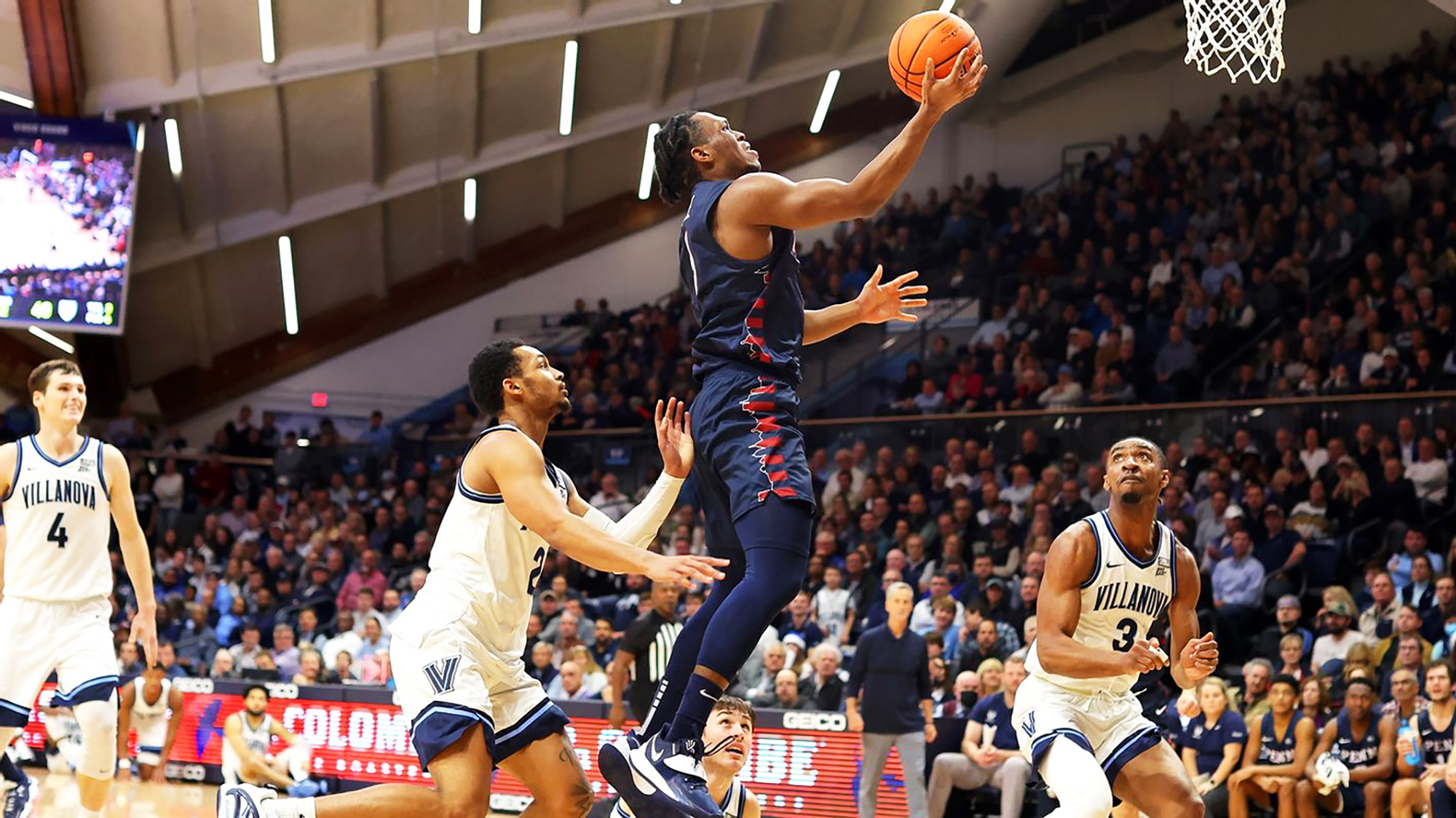 In the air above Villanova defenders, Dingle drives to the basketball with a large crowd watching.