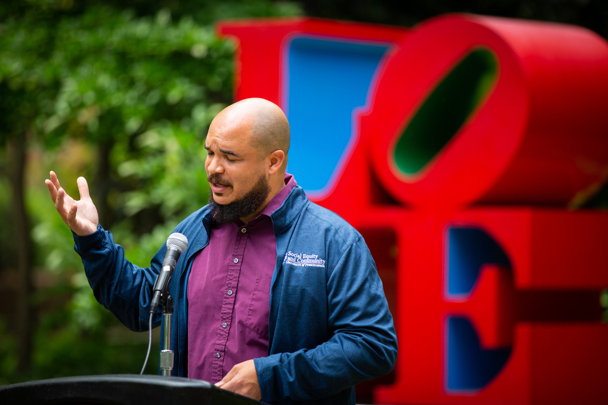 Chaz Howard speaks into a microphone in front of the LOVE statuee