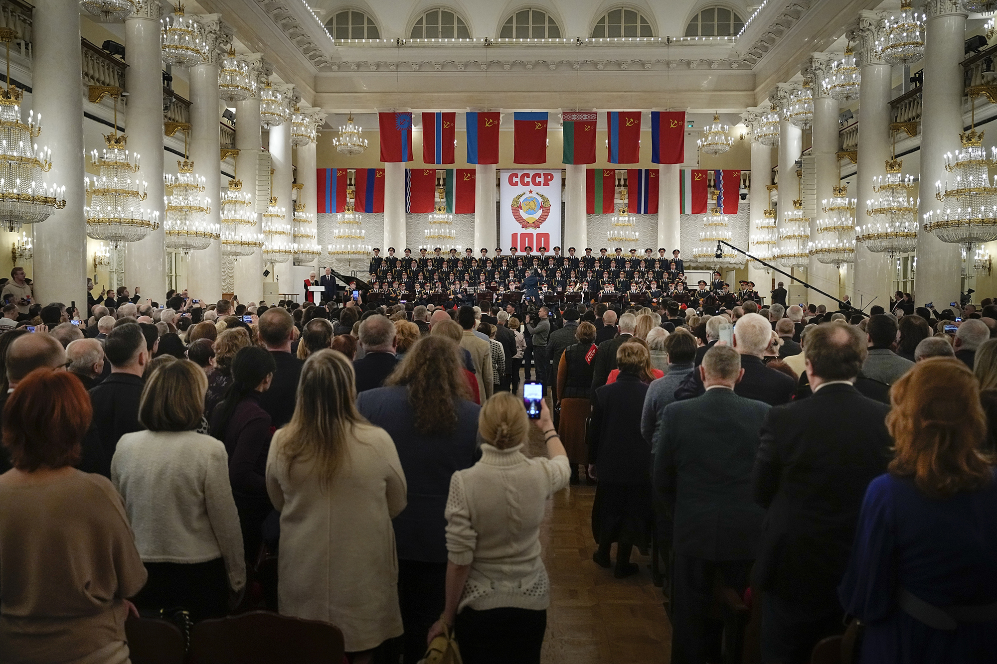 People listen to singers perform the Soviet anthem in a hall lined with columns and chandeliers