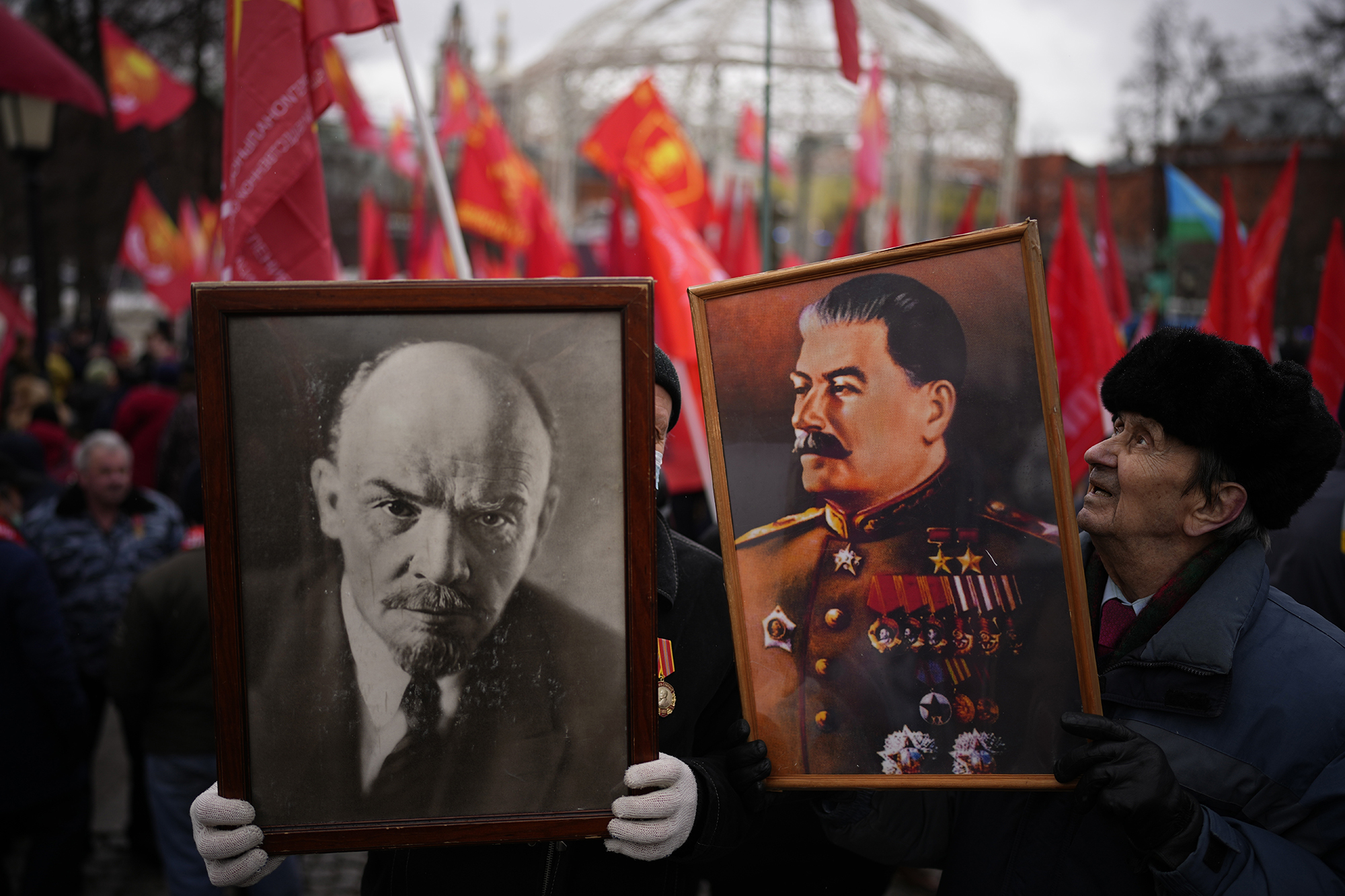 One person holds a framed image of Vladimir Lenin and another holds one of Josef Stalin as others wave red flags behind them in Moscow's Revolution Square.