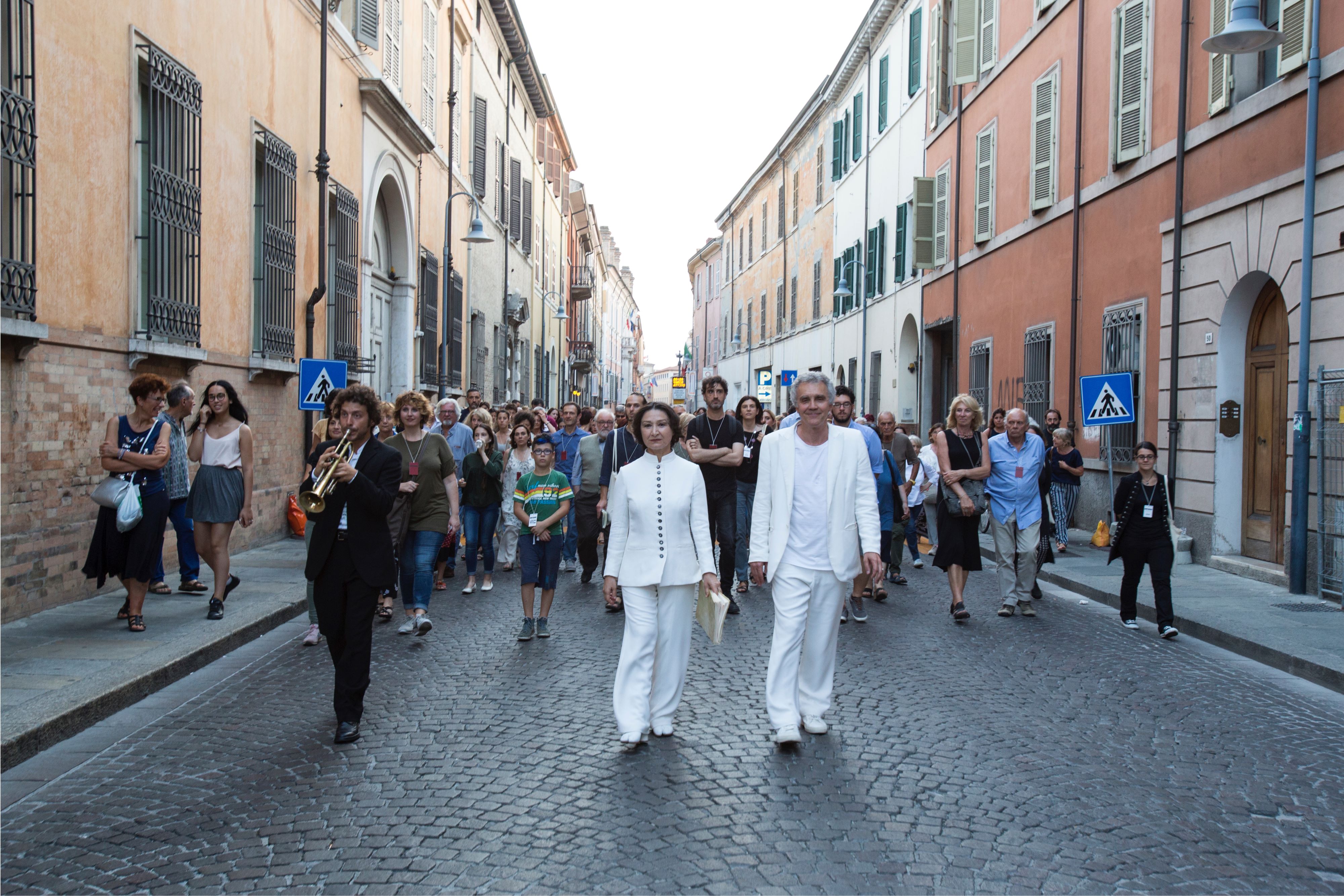 Two people dressed in white lead a procession through an Italian city street