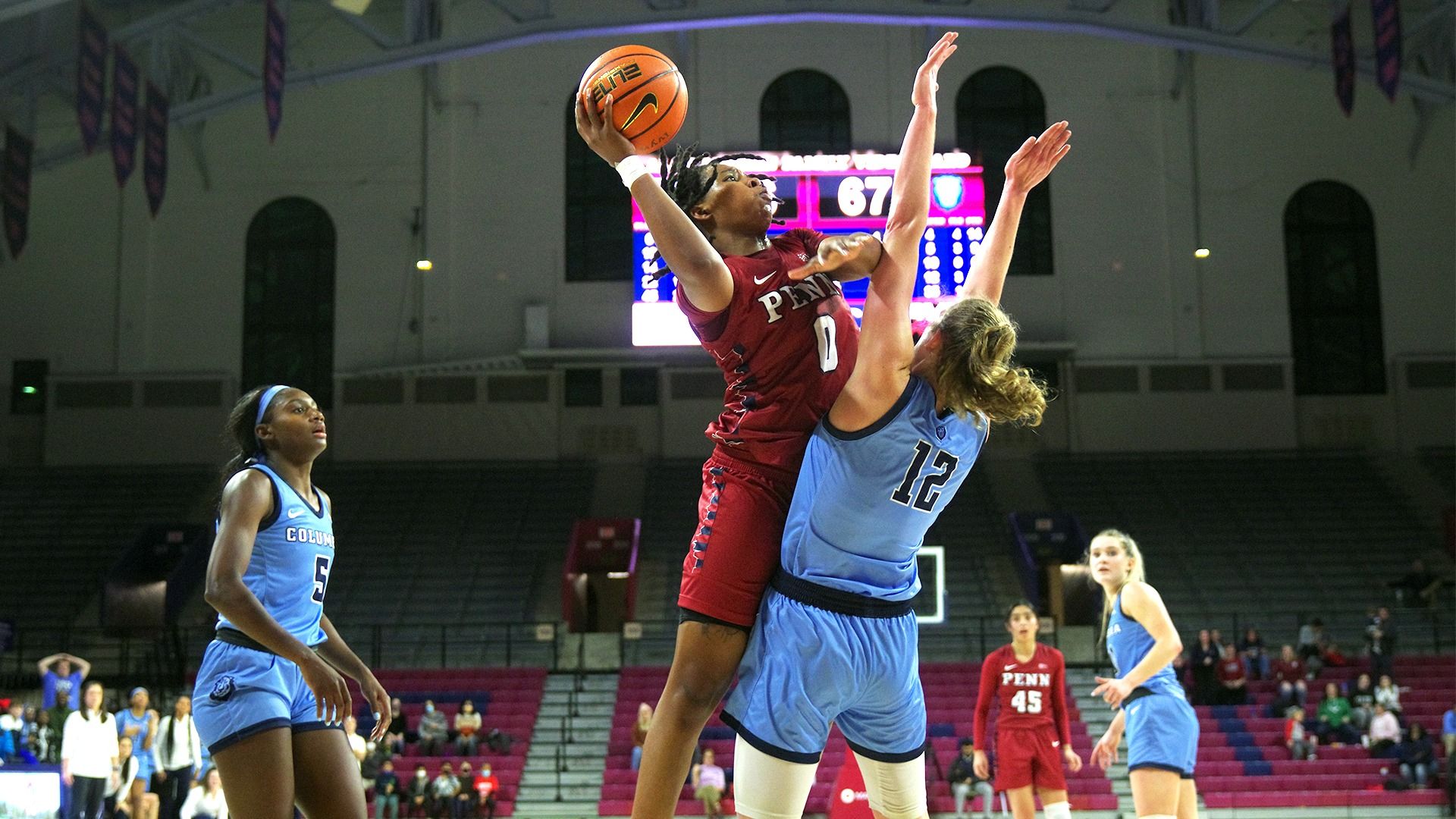 Holding the ball in the air over her head, Obi takes a shot while a Columbia defender guards with both arms up at the Palestra.