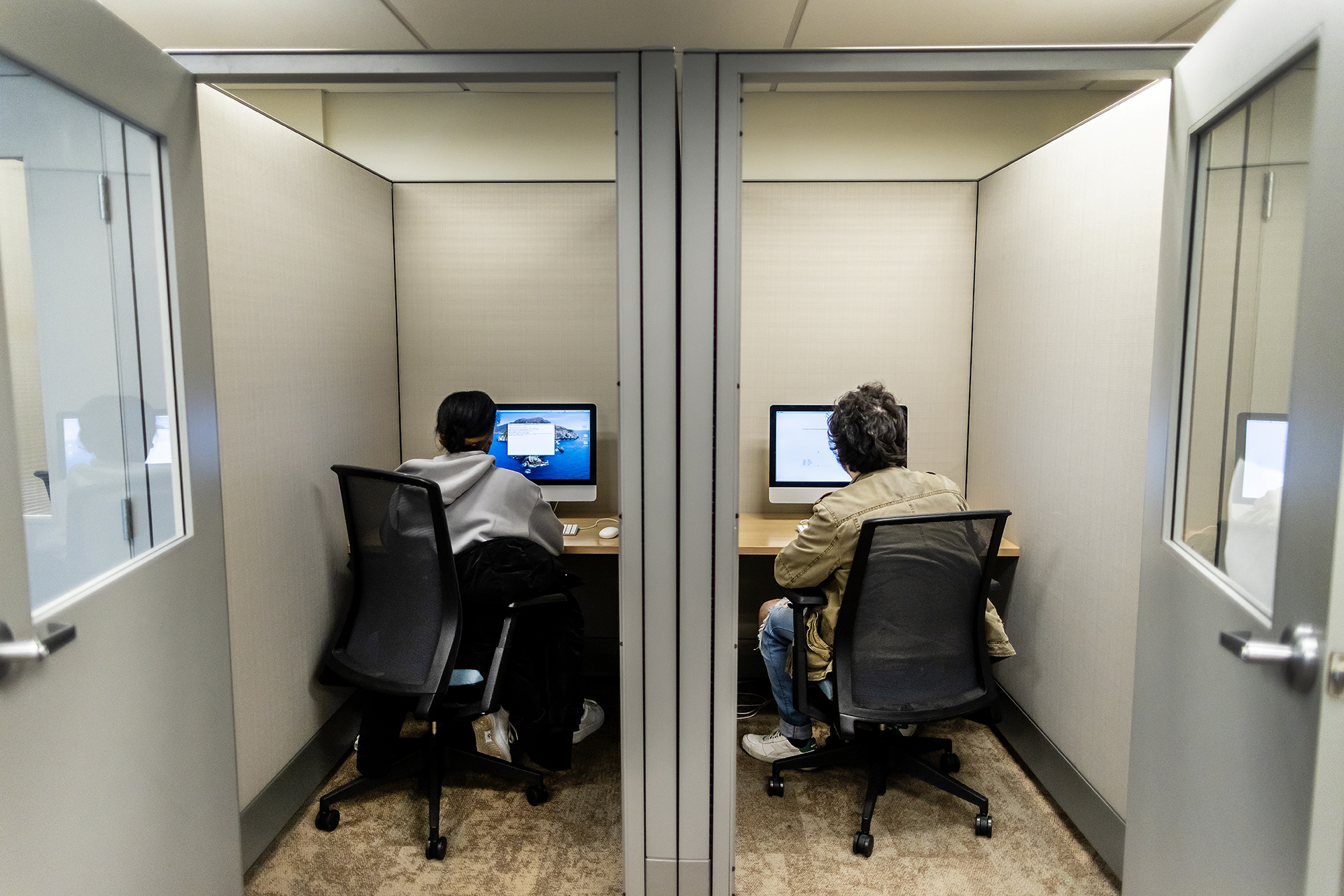 Two people at desktop computers in language lab booths side by side.