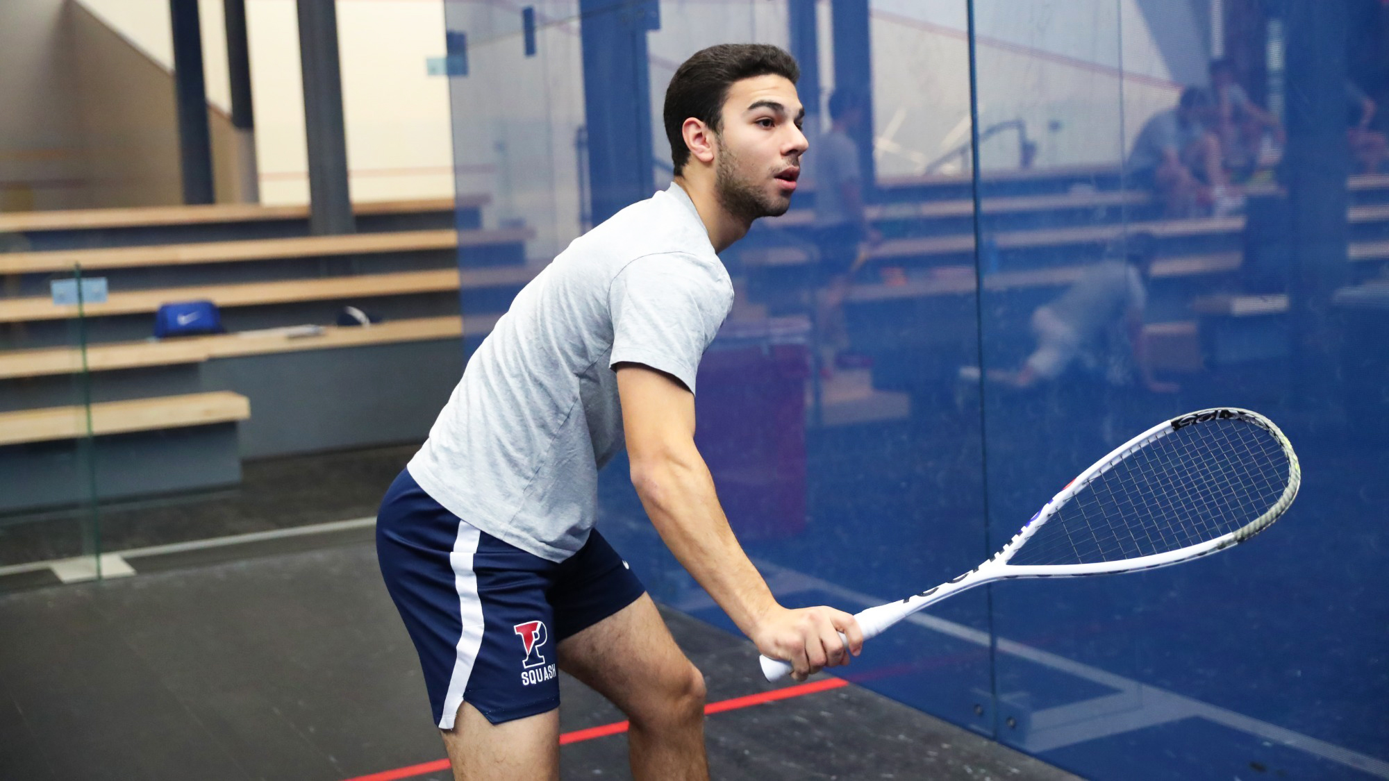 Hafez in a squash court with a racquet in his hands ready for a shot.