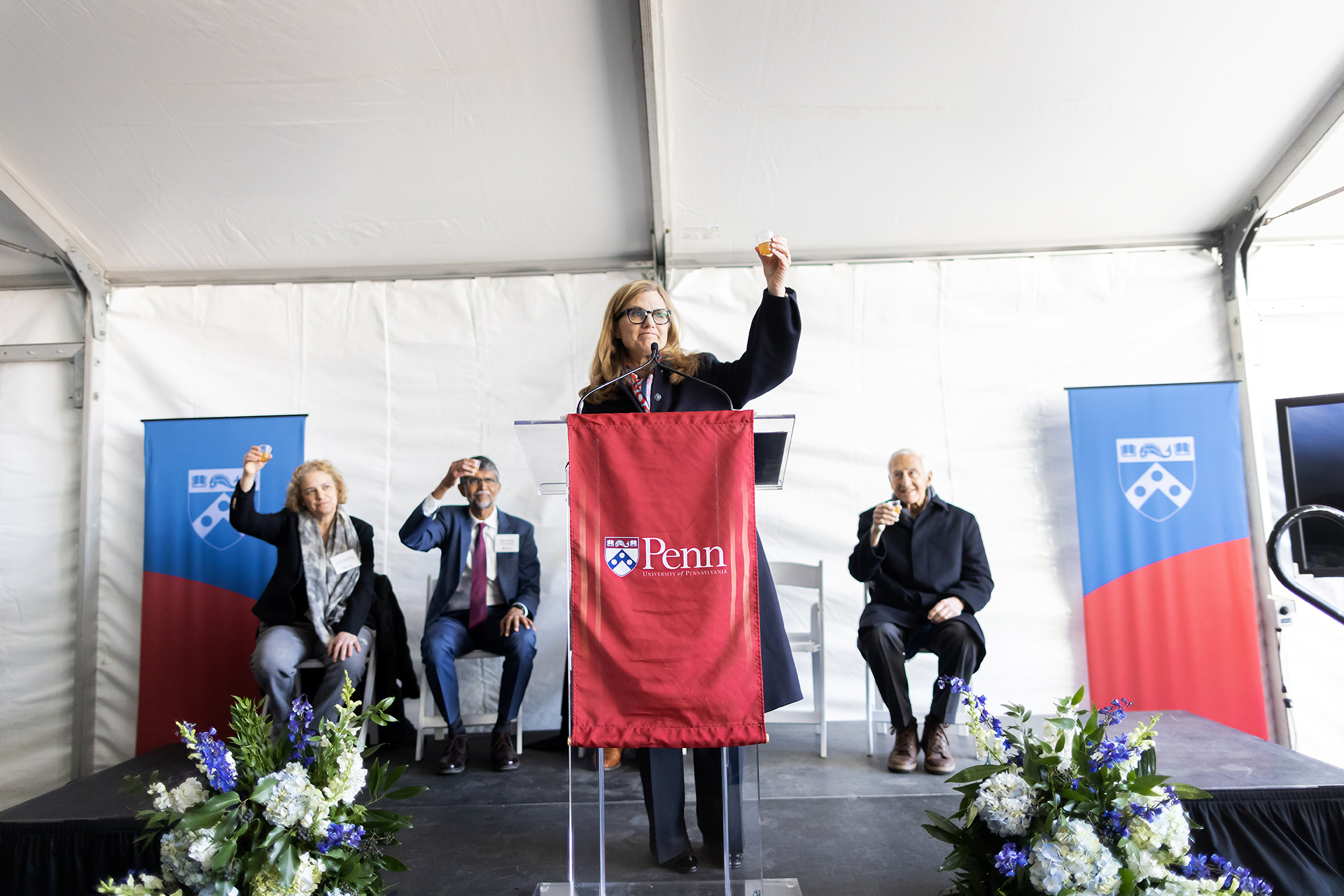Penn President raises a glass in a toast while speaking at a podium at the Vagelos topping off ceremony.