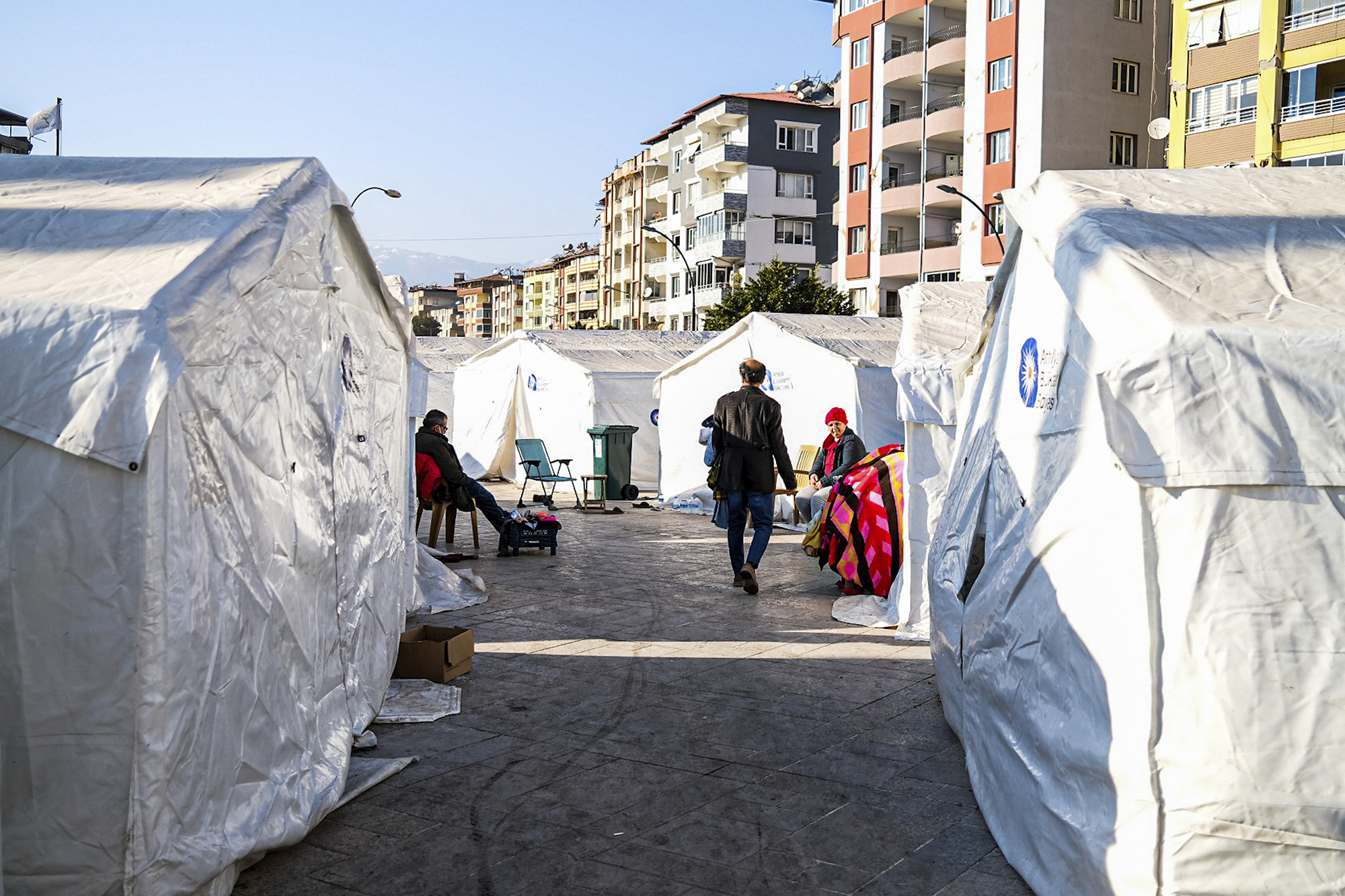 Temporary shelters erected as a place for injured to received assistance. Two people sit outside, and a third walks toward them.