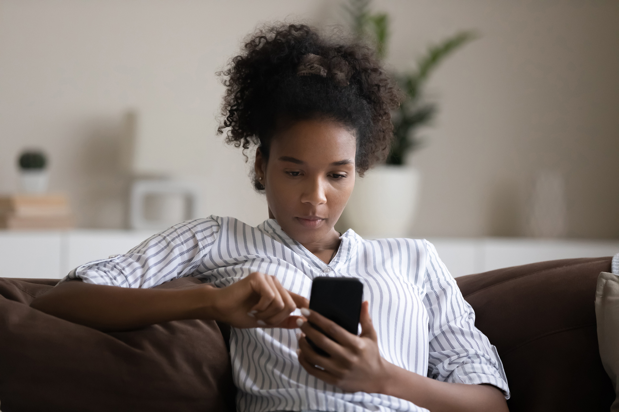 African American person using a smartphone on a couch.