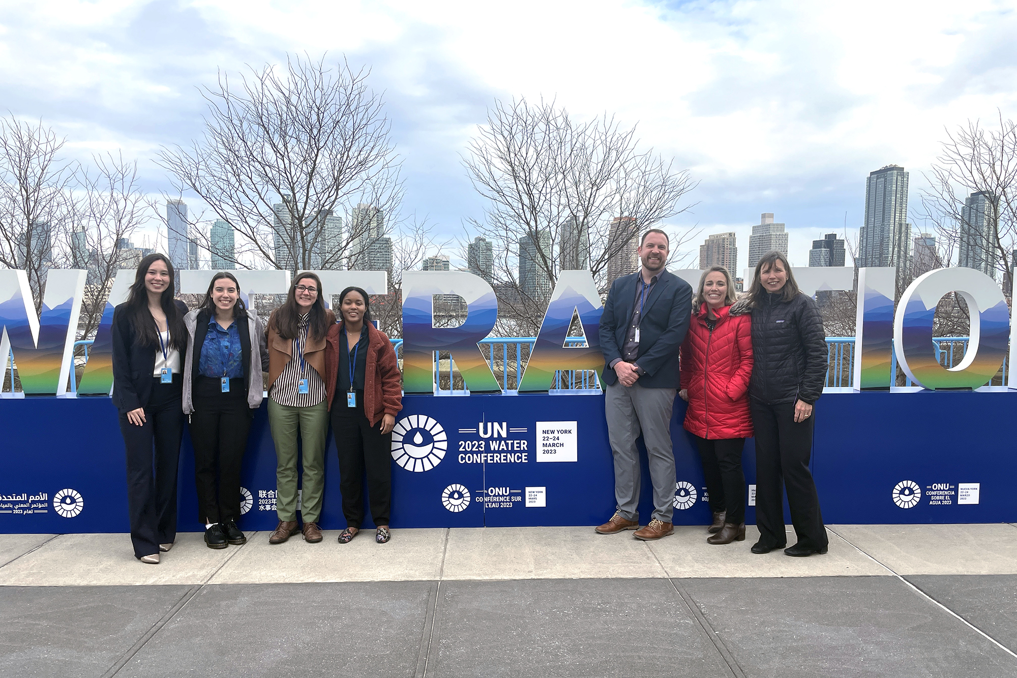 Seven people stand in front of banner reader UN 2023 Water Conference with New York skyline in background