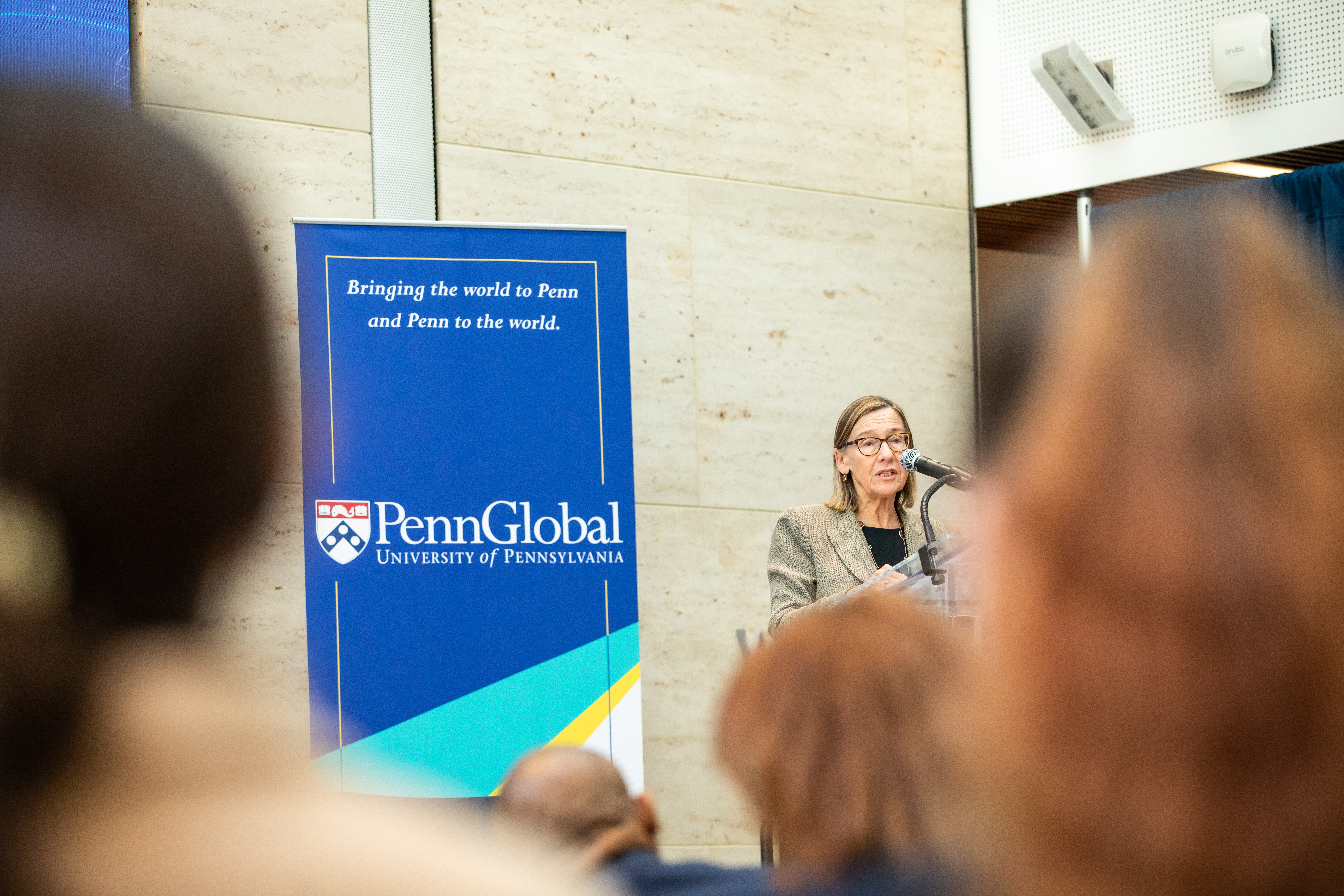 Dean Pam Grossman speaking at podium with sign behind her that says PennGlobal