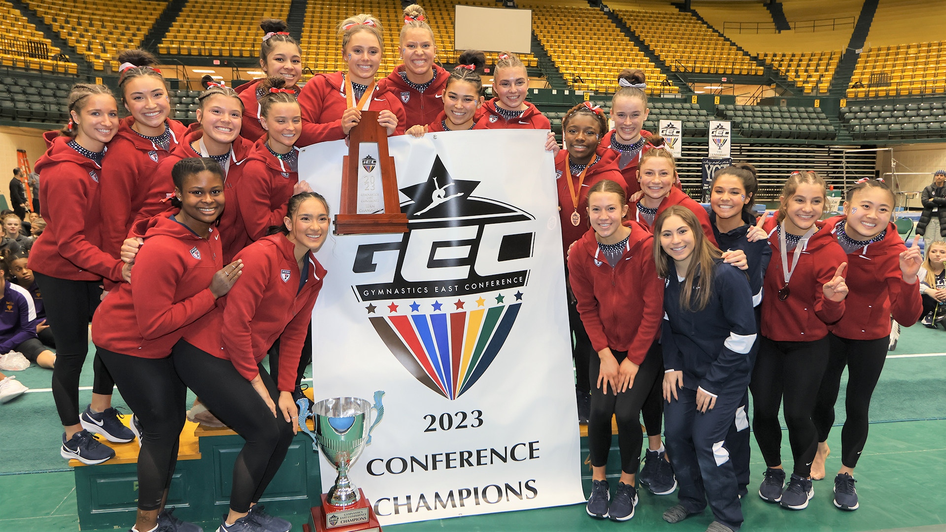 the gymnastics team members pose with trophy and GEC 2023 conference champions banner.