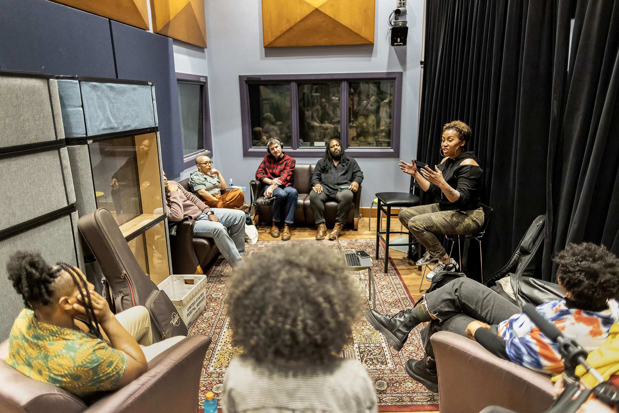 A person on a stool speaks with seven people seated in an office at WXPN.