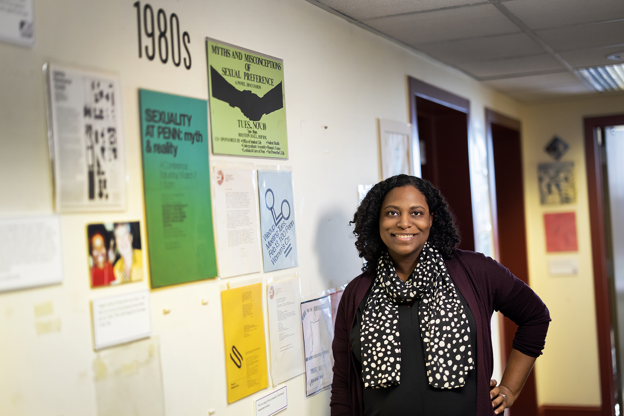 Elisa Foster stands in the Penn Women's Center Hallway, which contains a display of flyers that showcase the Center's history. Here, the 1980s. 