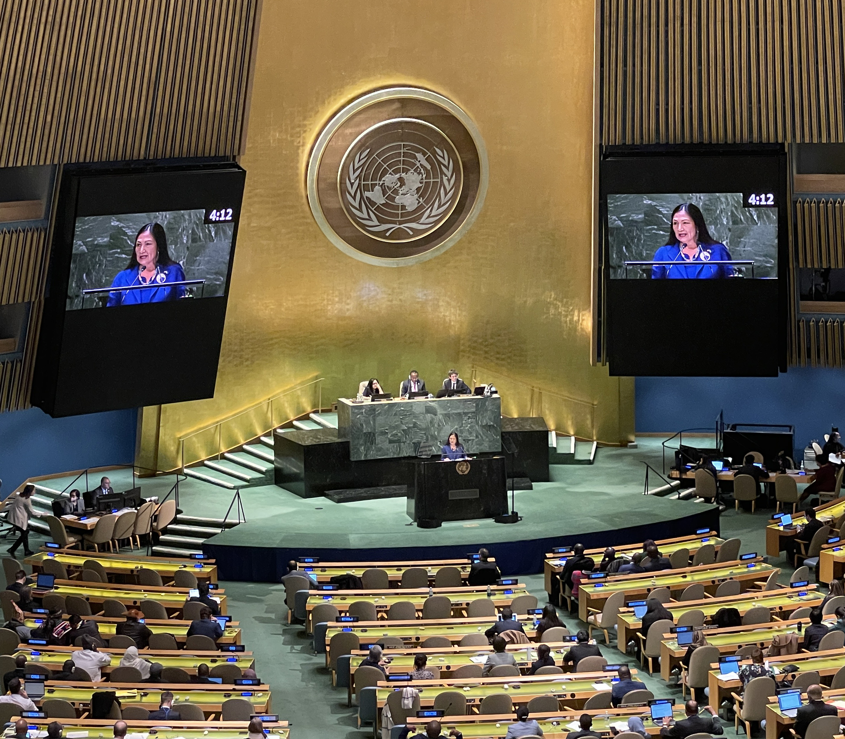 In a large auditorium in front of UN logo, a speak addresses the audience