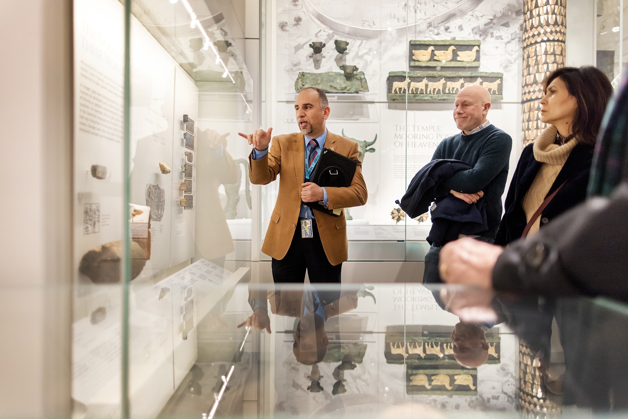 Yaroub Al-Obaidi gestures to artifacts in the Penn Museum's Middle East Galleries while a group of visitors looks on.