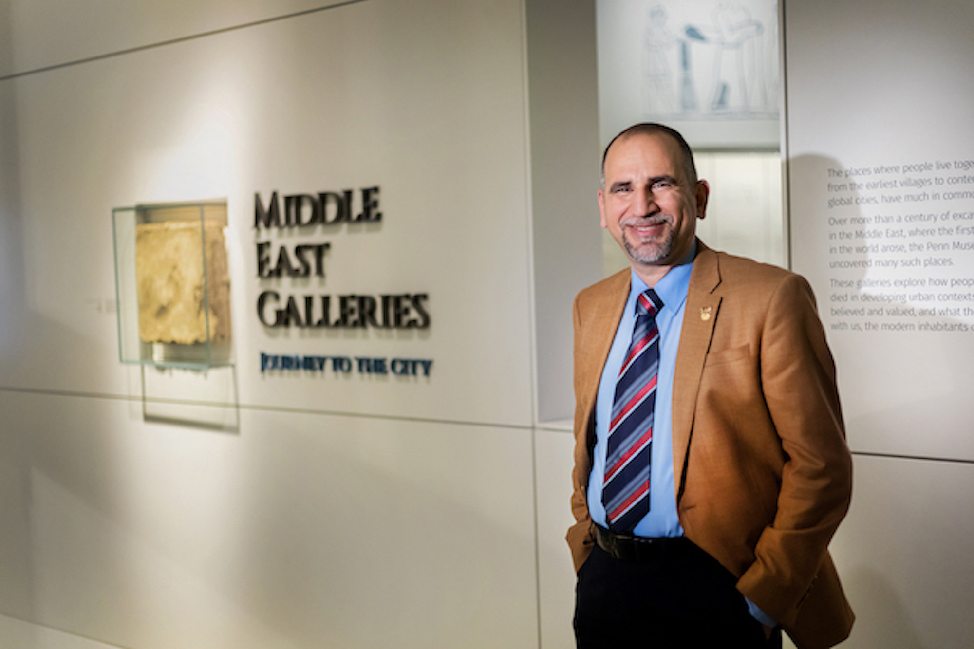 Yaroub Al-Obaidi stands in front of a sign reading Middle East Galleries inside the Penn Museum.