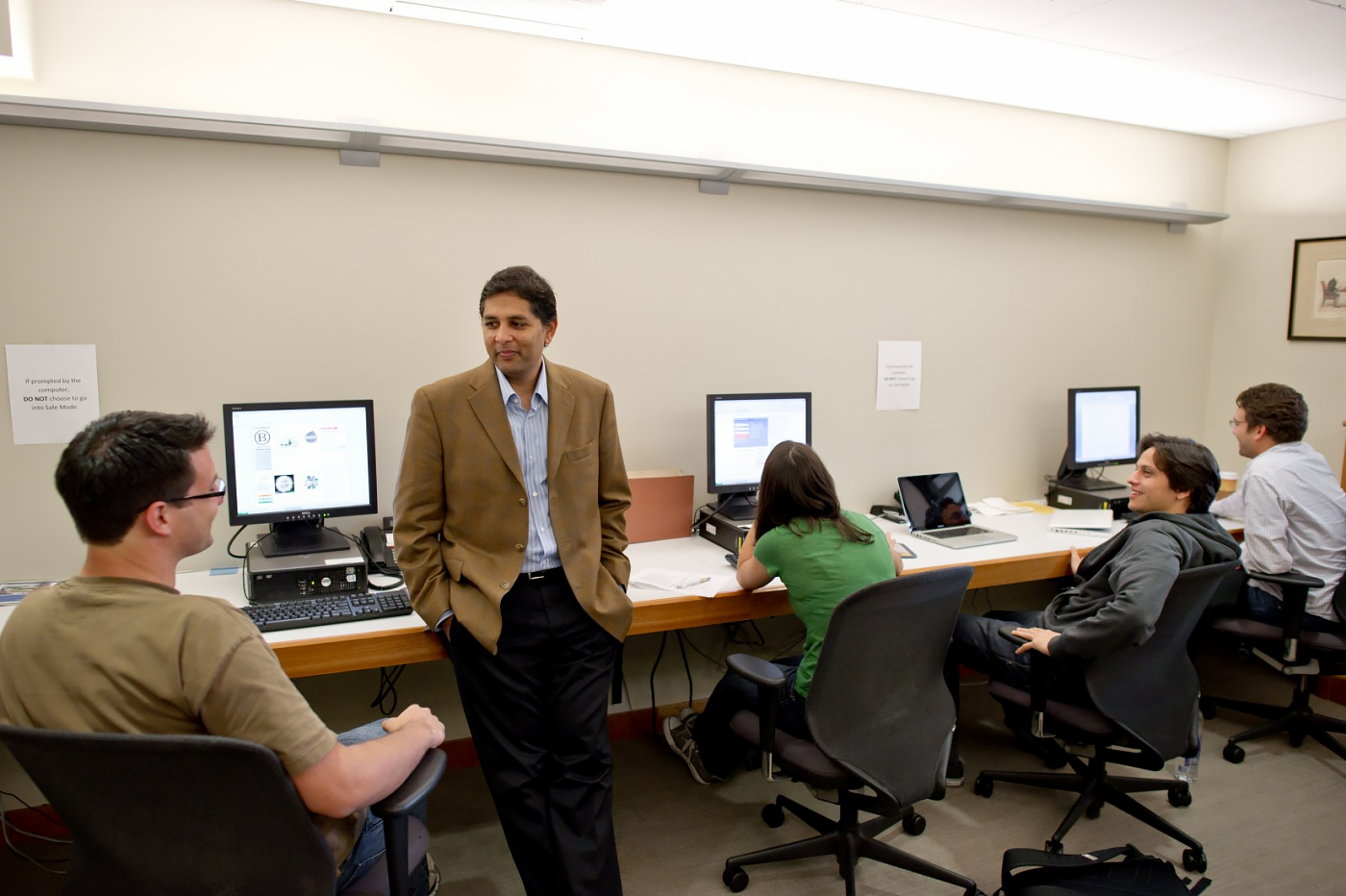 Praveen Kosuri (standing) talks with four students at desktop computers.
