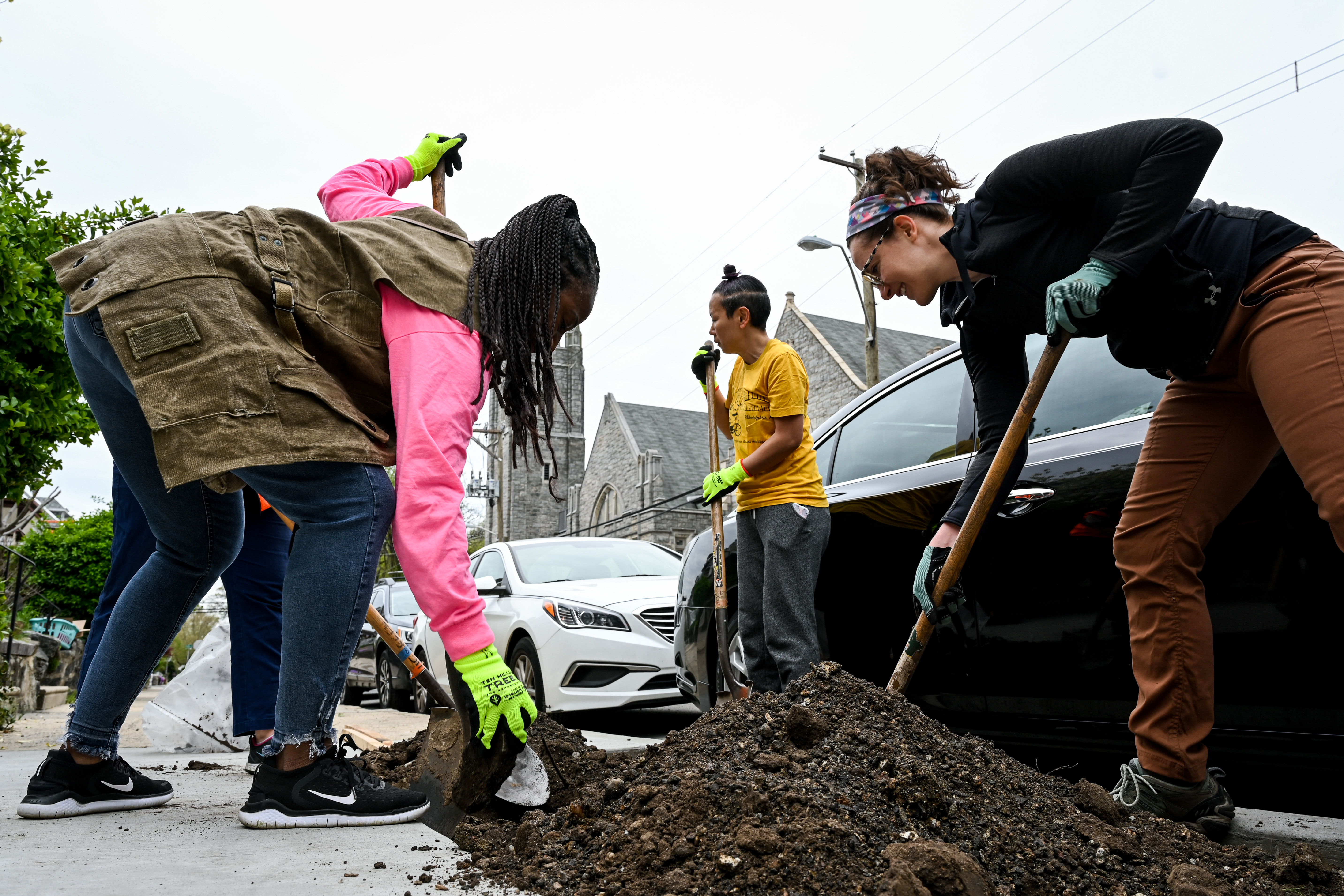 People dig in the soil along a sidewalk in preparation for planting a tree