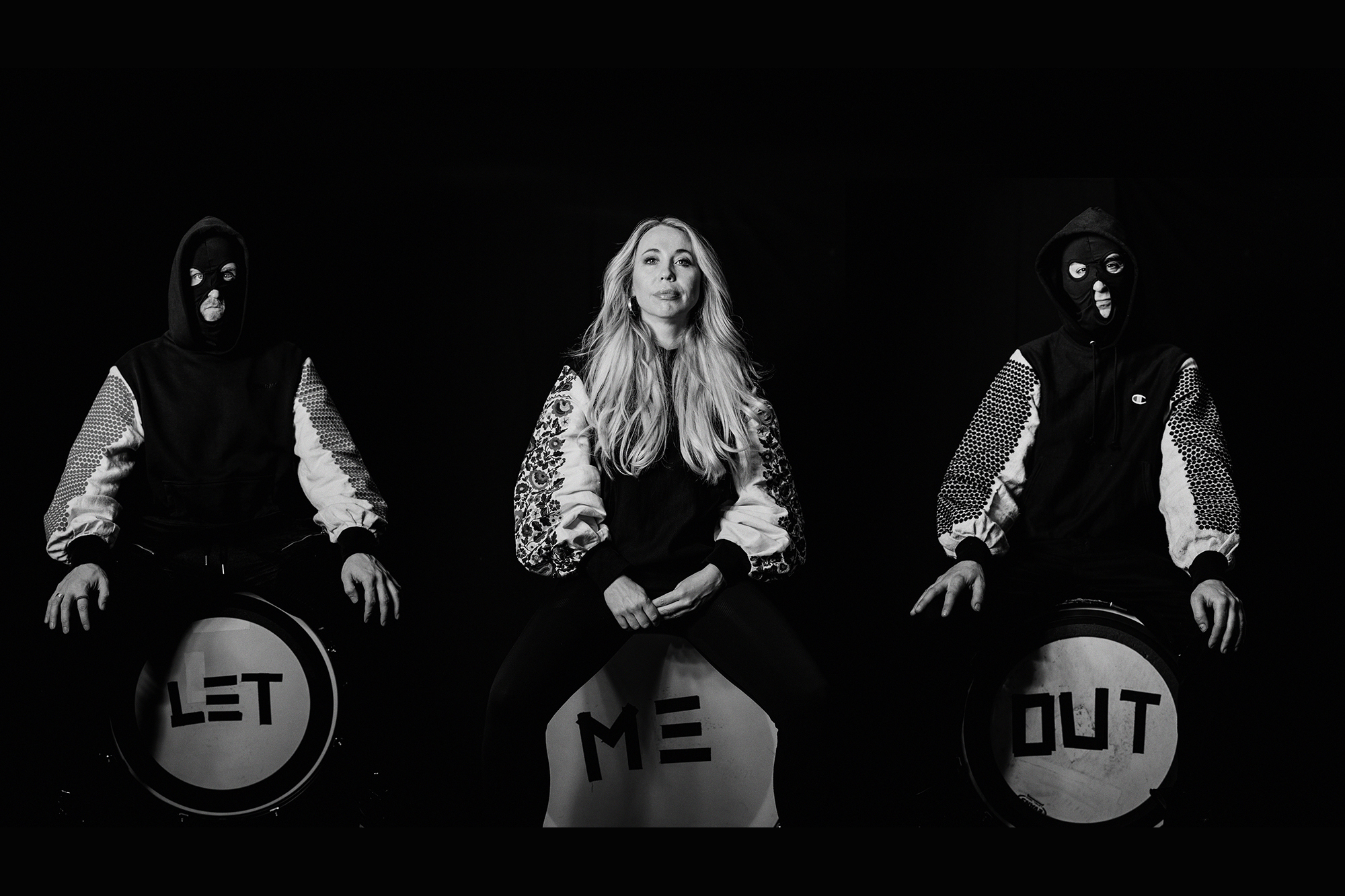 Three artists hunched over signs that read "Let me out."