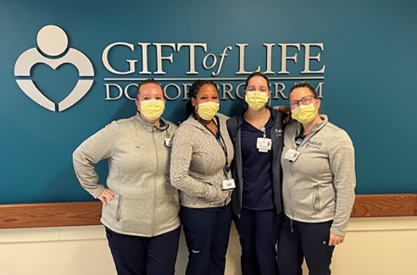 Leah Lambe and three members of Penn Medicine in front of a sign on the wall reading Gift of Life Donor Program.