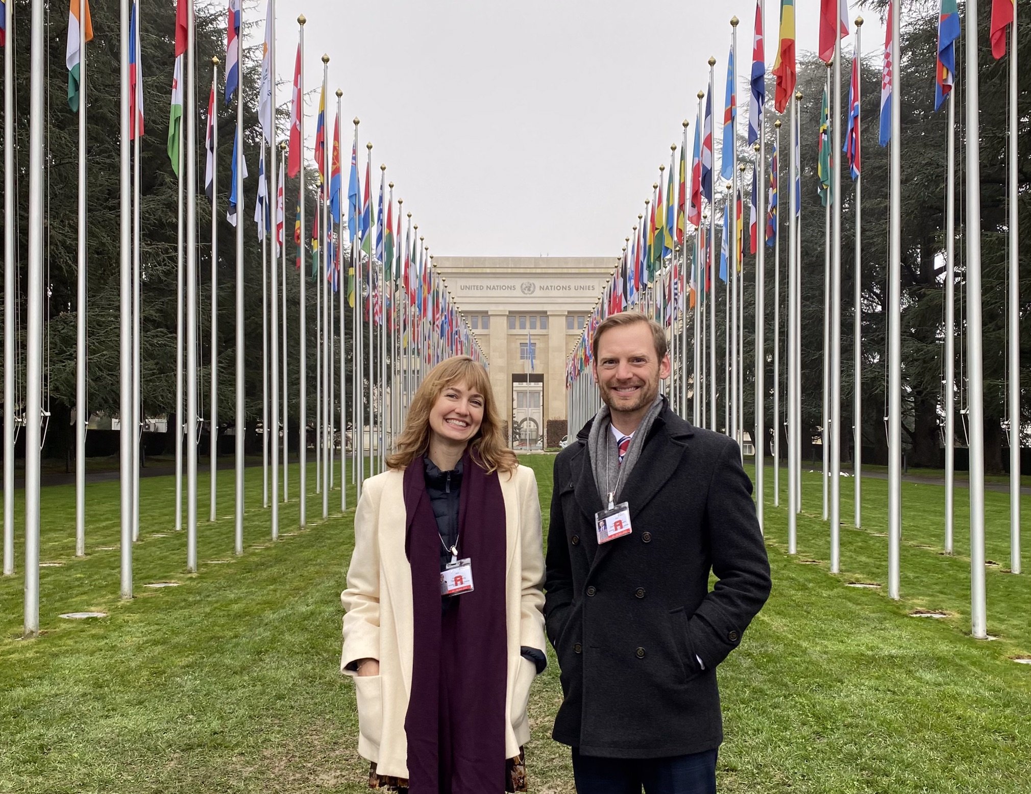 Taylor Hausburg and Zachary Herrmann stand in front of a line of flags at the United Nations headquarters in Geneva