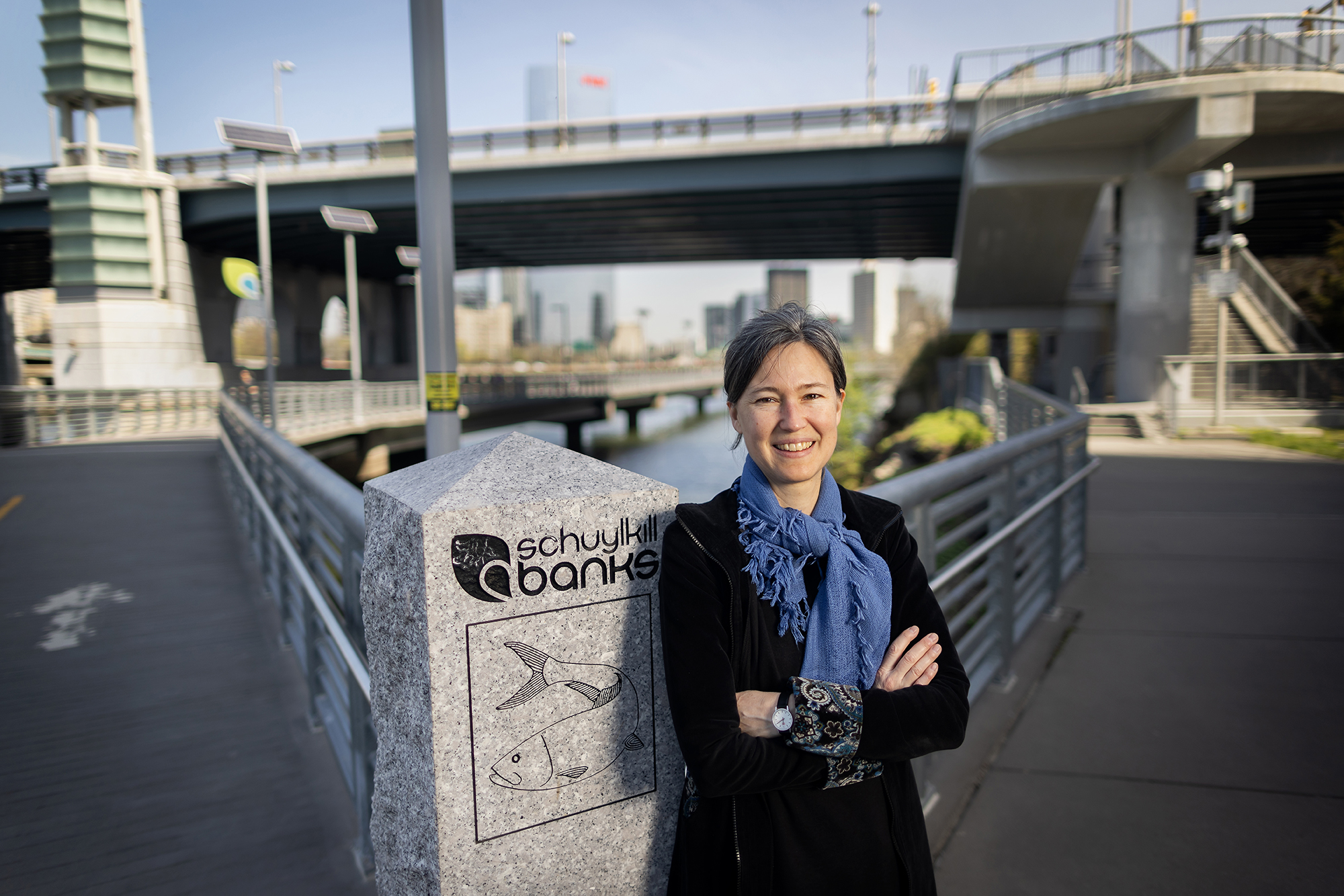 Sonja Dumpelmann with arms crossed against a stone pillar with a carved fish that reads "Schuylkill Banks"