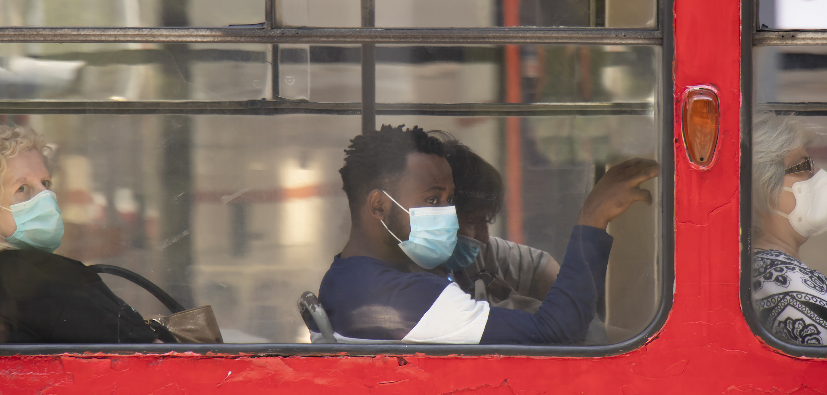 Young black man wearing surgical face masks while sitting and riding on a window seat of a tram