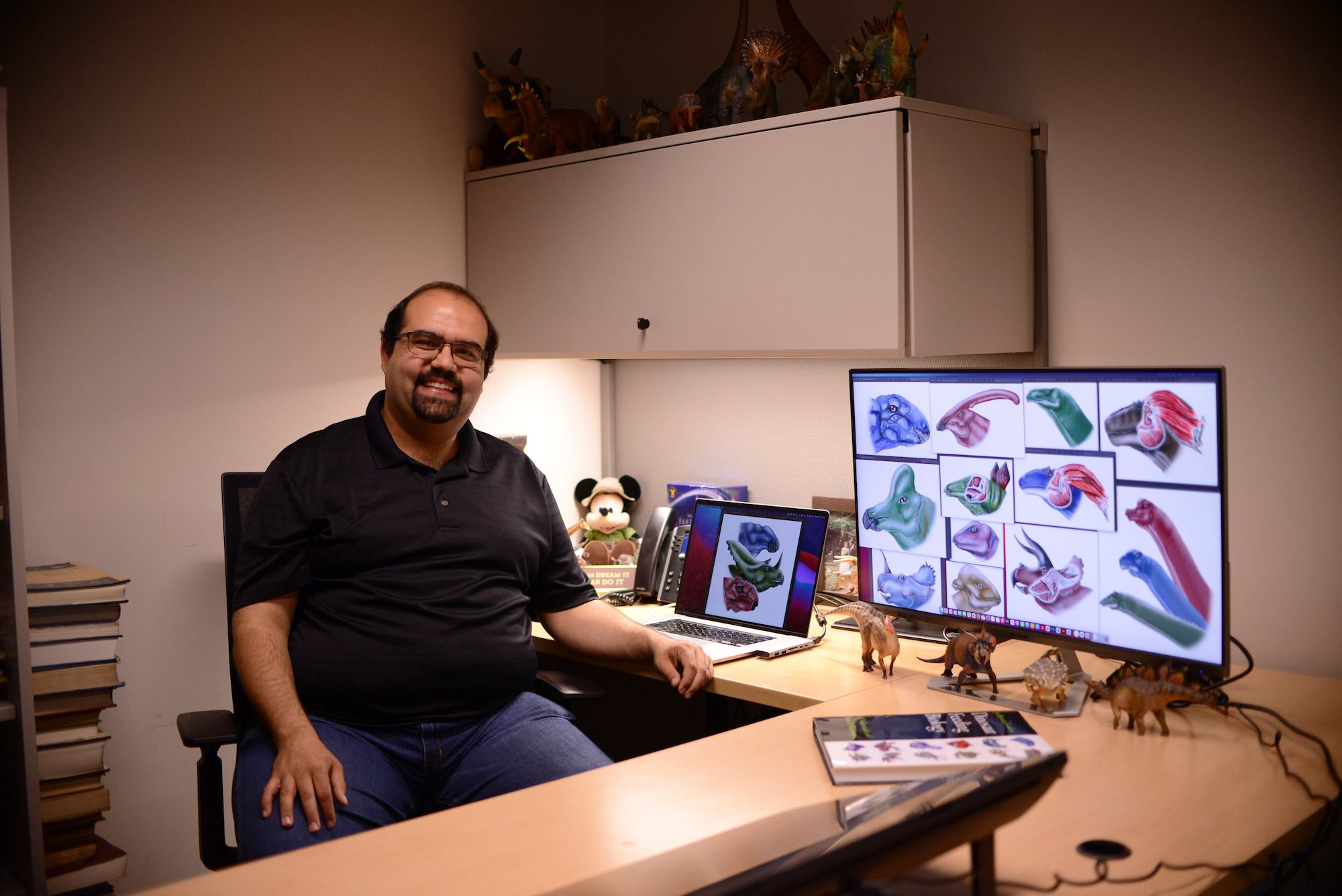 Paleontologist Ali Nabavizadeh in his office with dinosaur drawings on the computer