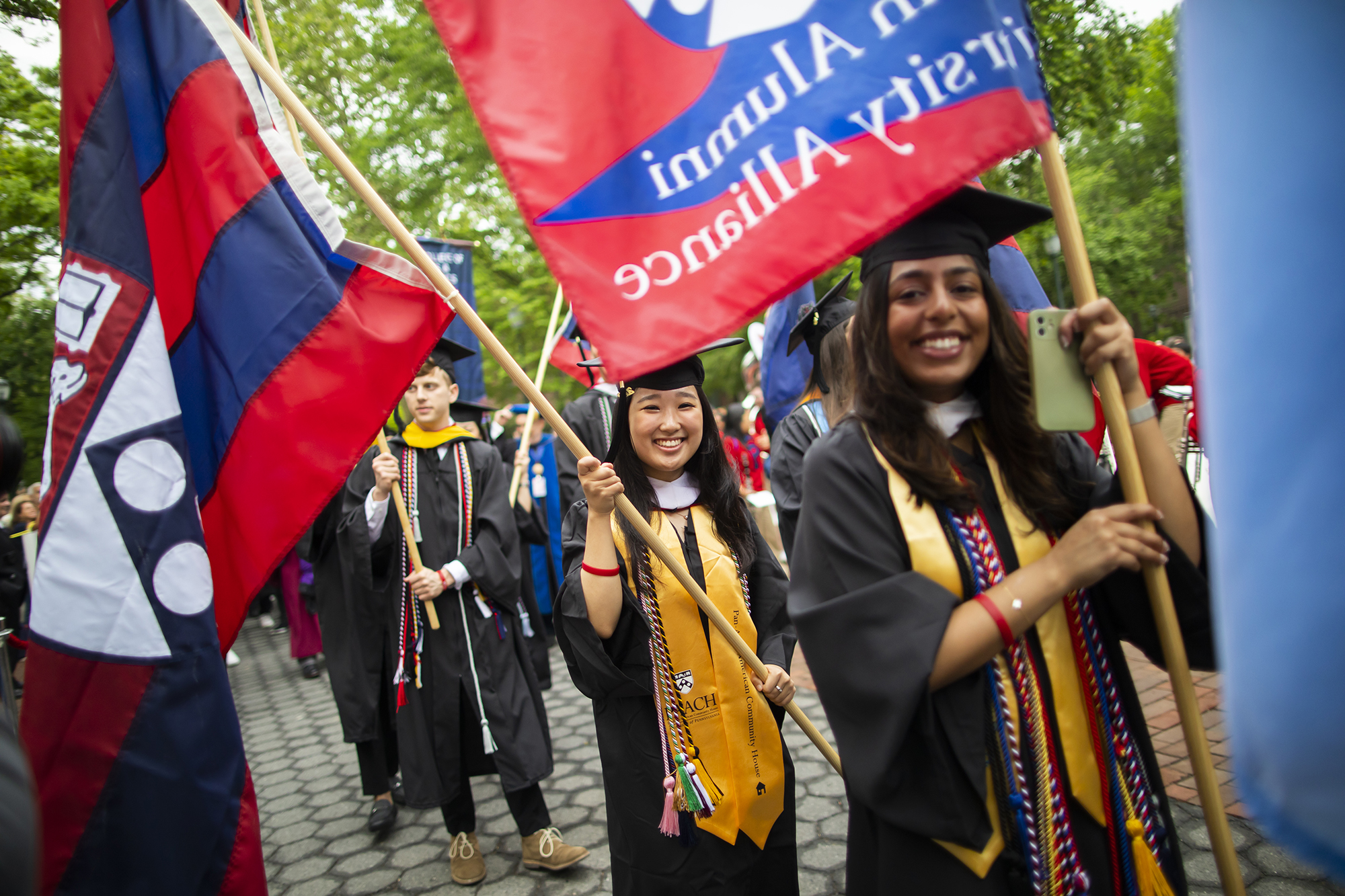 Procession of Penn grads on Locust Walk holding flags.