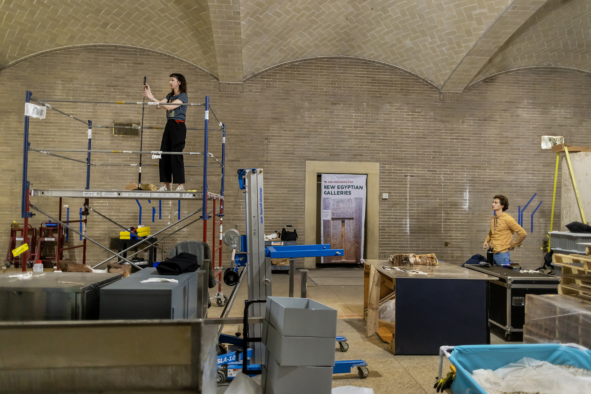 Molly Gleeson stands on scaffolding in the Penn Museum setting up VR equipment.