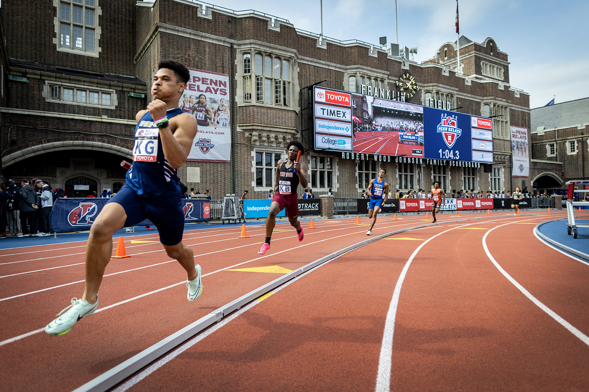 four relay runners with batons on the track