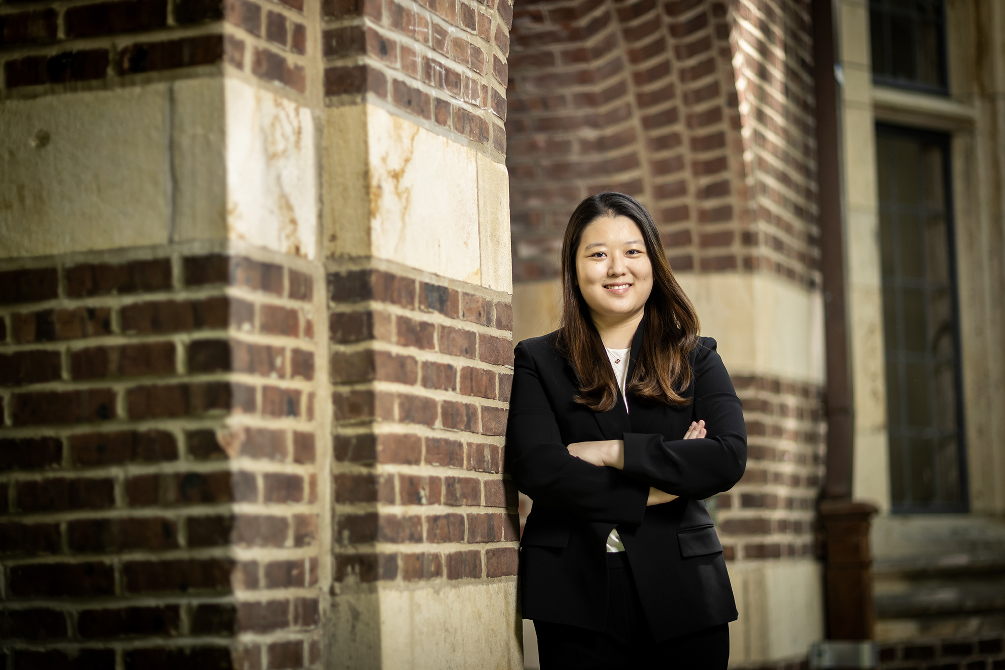 Lucy Lee stands with crossed arms against a brick archway