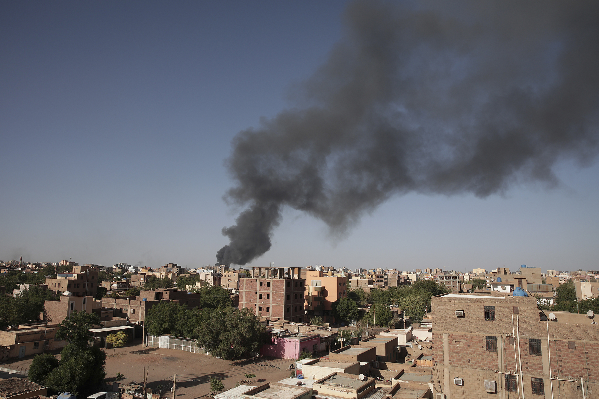 A view of the Sudanese capital of Khartoum shows brown buildings and dark grey smoke billowing against a blue sky.