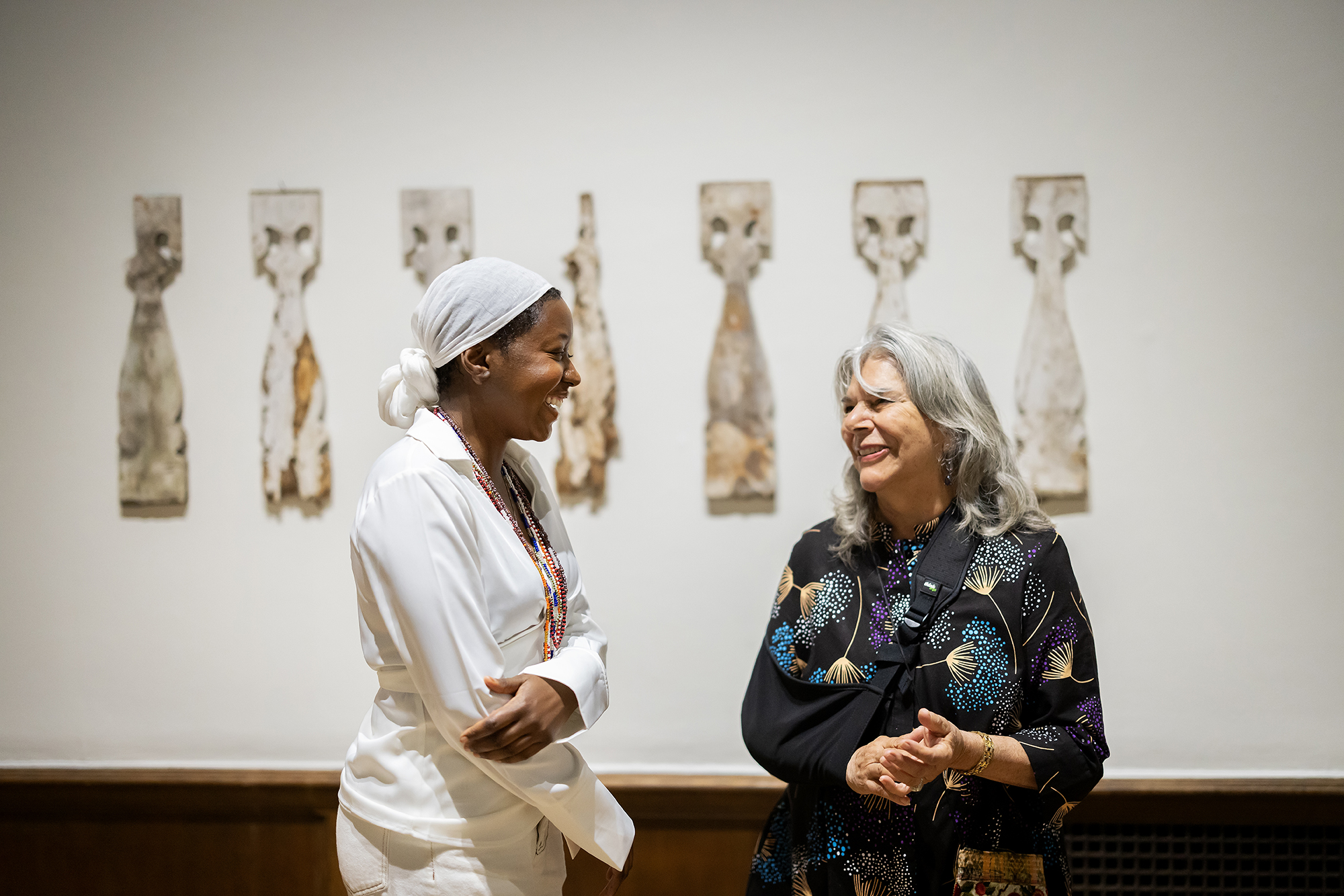 two artists laughing with each other standing in gallery in front of wooden balusters on wall