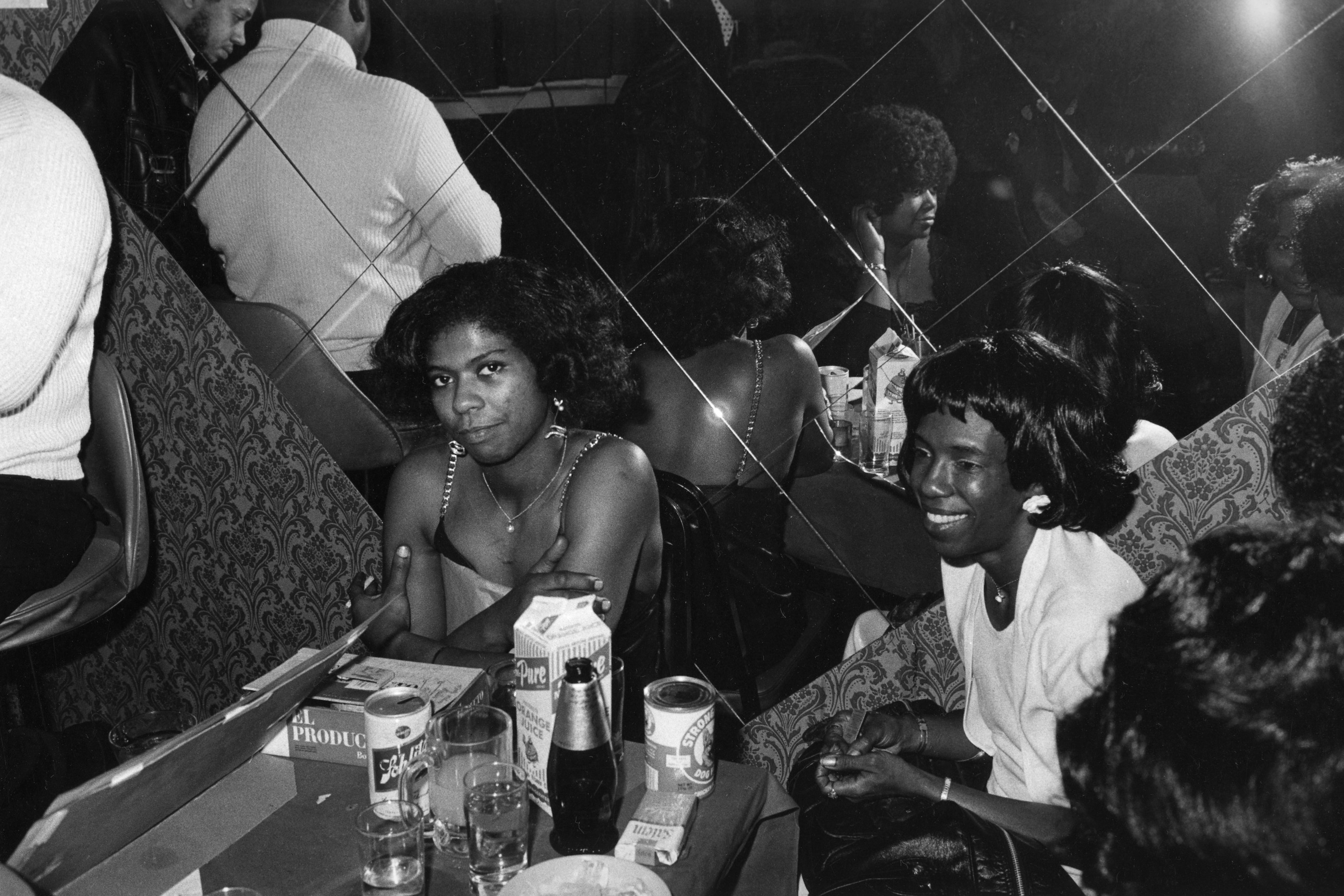 Clubgoers lounge in a bar with their reflections shown in a mirror behind them.