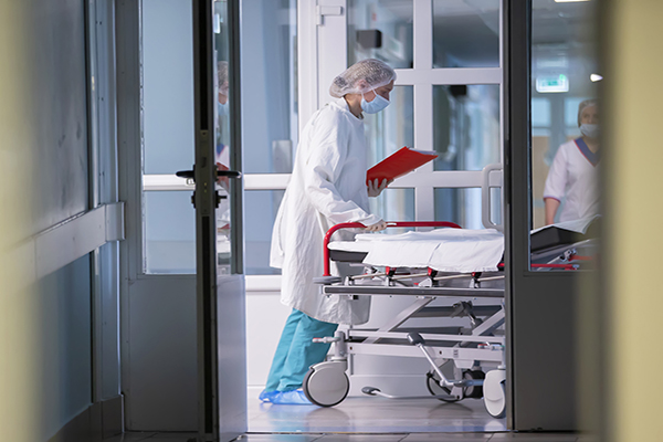 Person in scrubs wheeling gurney into a hospital