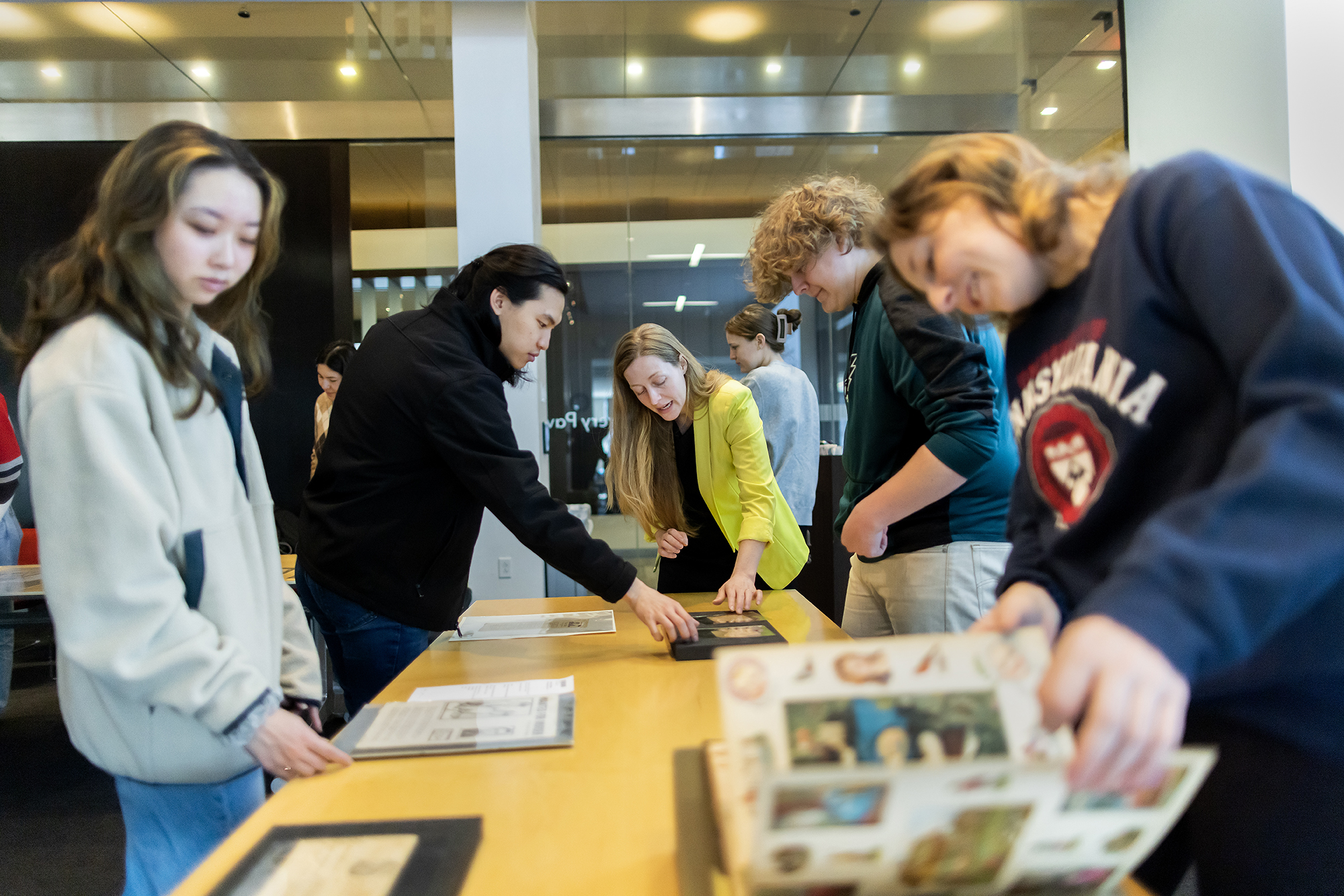 four students standing next to table looking at printed materials with professor