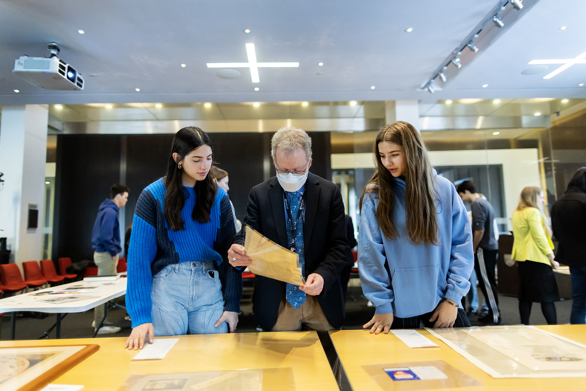 three people looking at a sheet of paper while standing at a table filled with printed materials