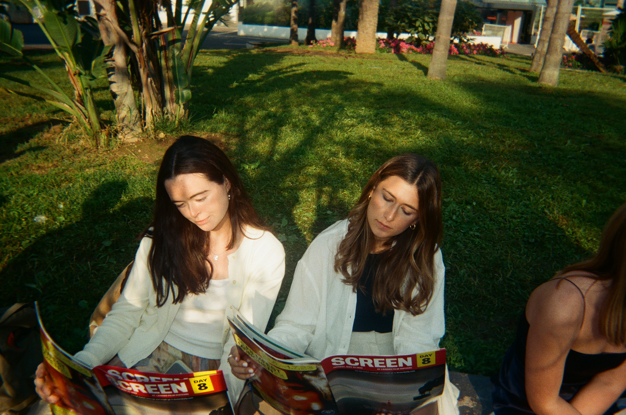 Isabel Sweeney and Drew Naiburg-Smith sitting on the grass together each reading a "Screen" Magazine