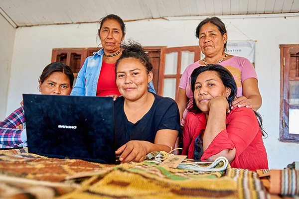 Five Matriarca artisans at a table sharing a laptop.