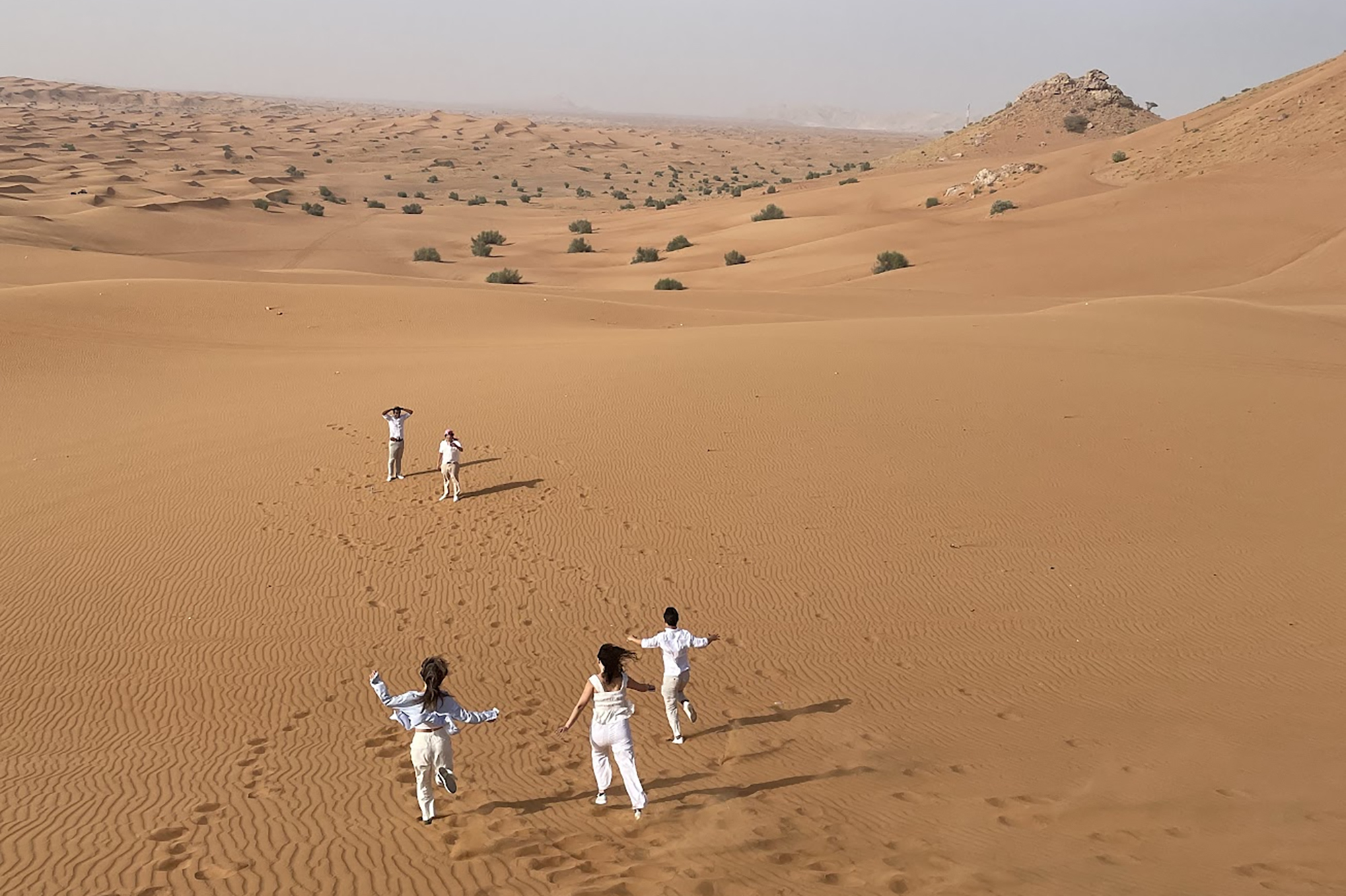 Five people running in the sand in a desert in the UAE.