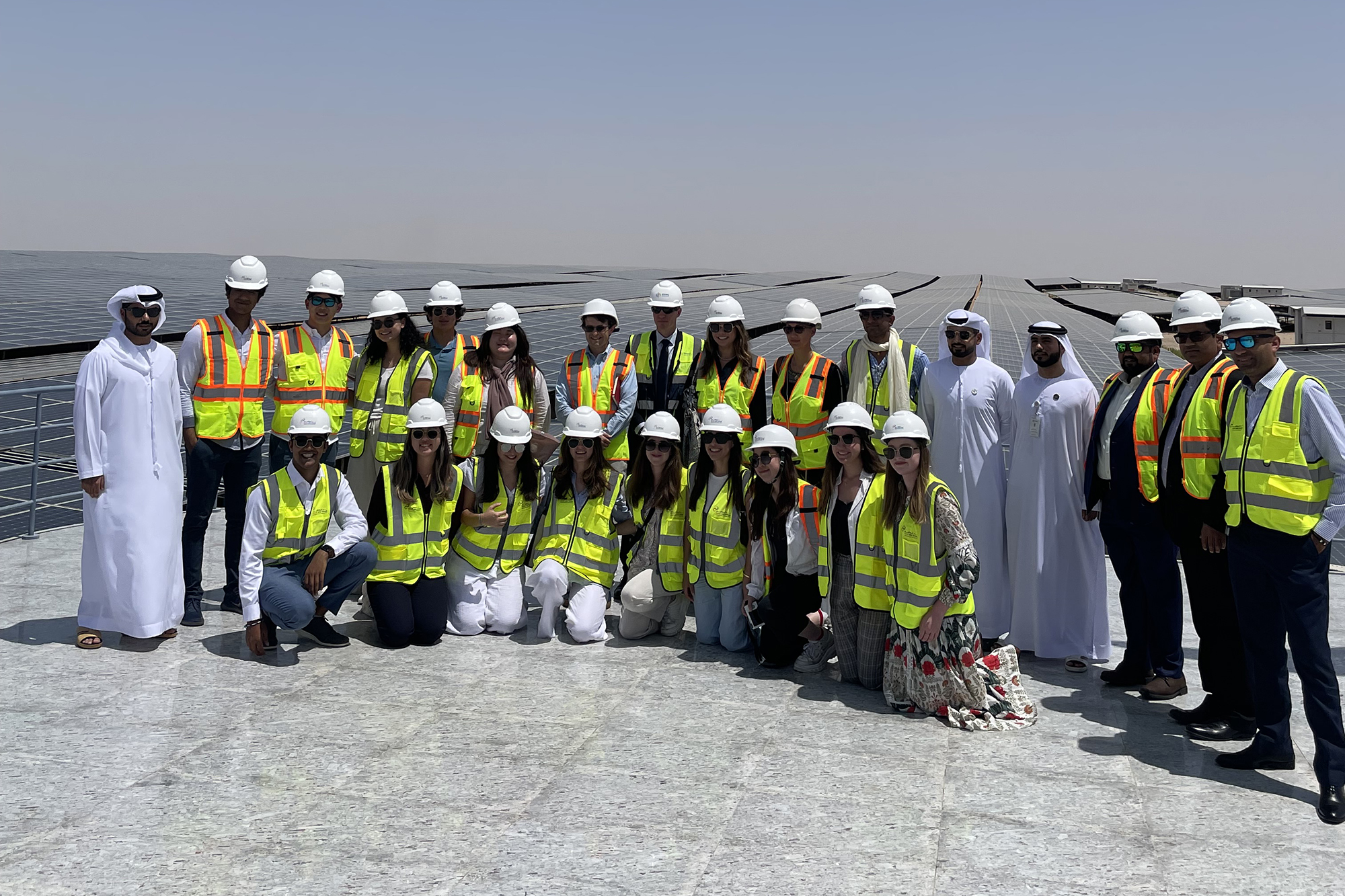 A group shot of students and officials in hard hats atop a roof of solar panels.
